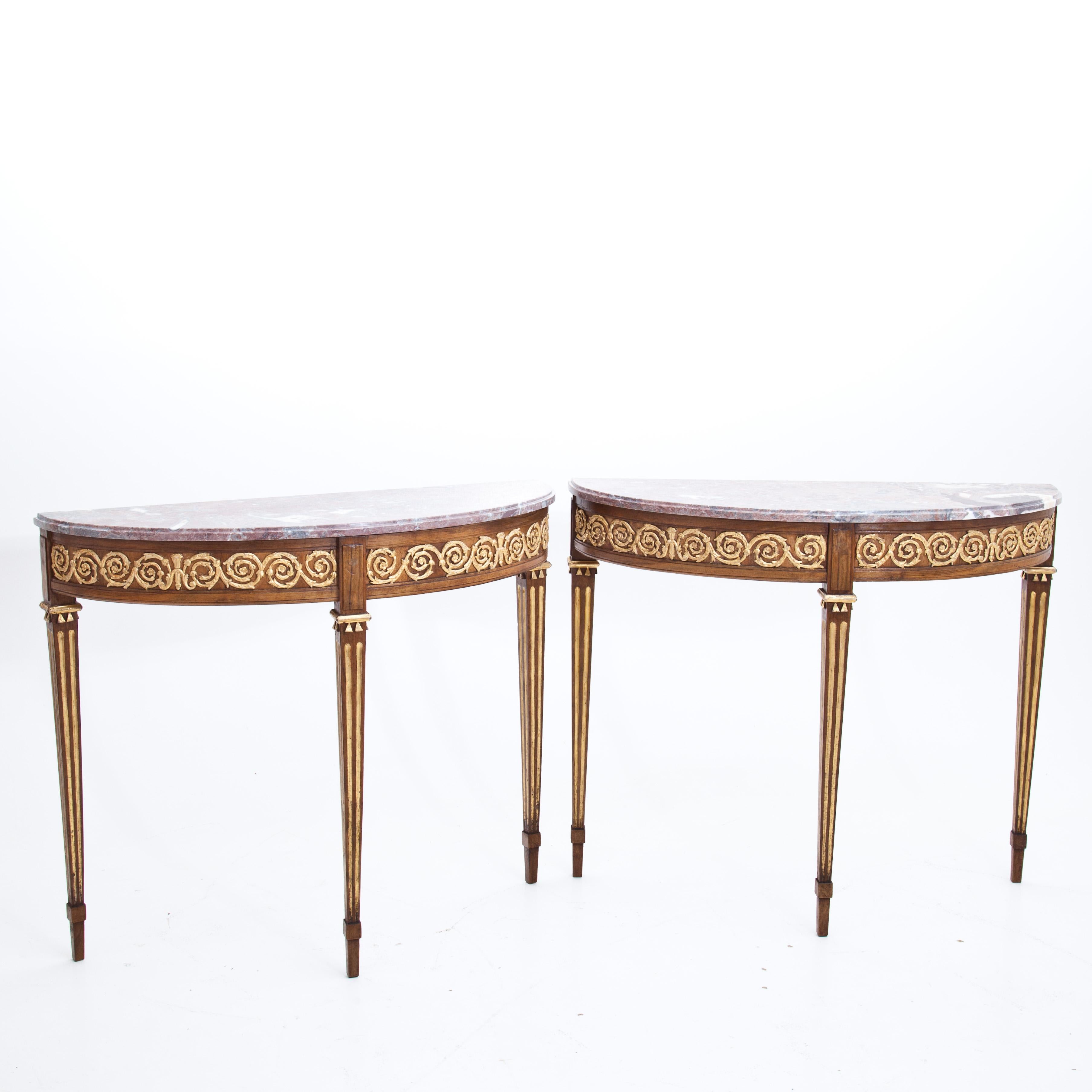 Pair of demilune consoles in solid walnut, on fluted square-tapered feet, with red marble tops and gilded, stuccoed meandering ribbon of tendrils on the sides. The consoles were redesigned using old parts. The marble tops are recent. Partly