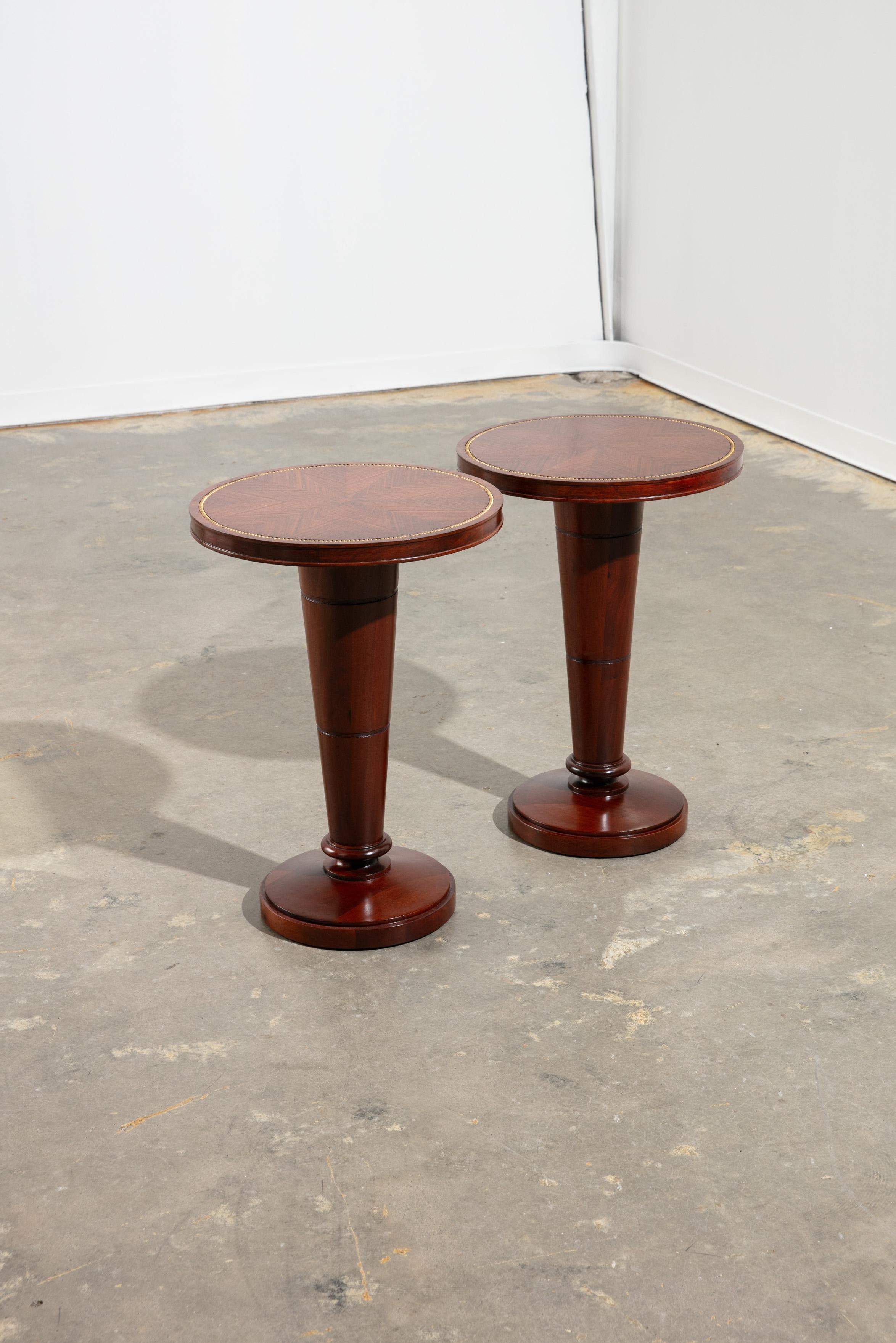 Pair of refinished 1940's mahogany round side tabloes/gueridons with a satin finish. Stunning geometric starburst wood pattern to the tops, with a decorative gold beading along the edge of each tabletop. Supported by a tapered pedestal base, resting