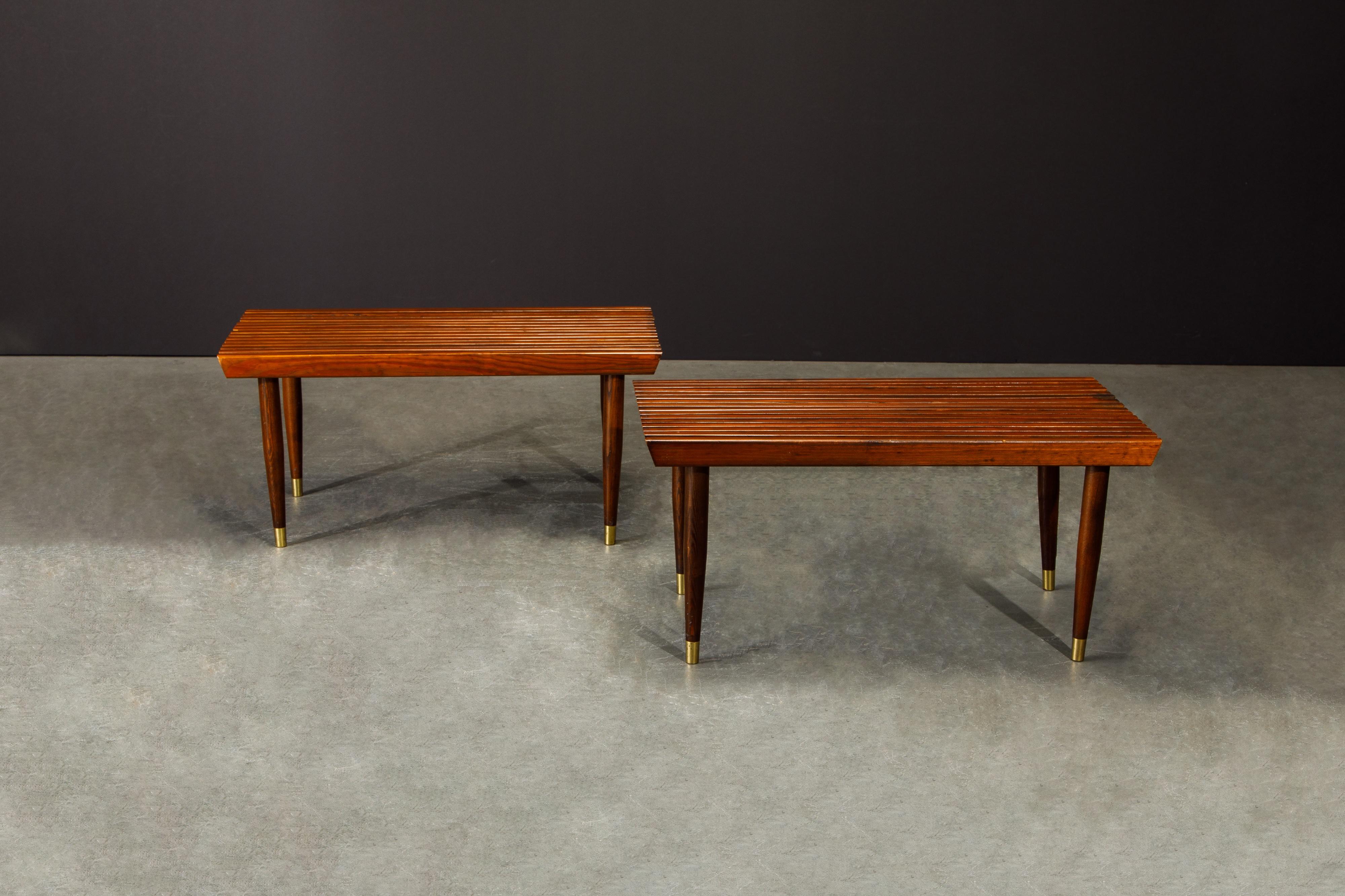 This lovely pair of Mid-Century Modern slatted wood benches which can also double as a coffee tables or low console tables have been refinished and features rows of slatted wood and four tapered legs which end in brass sabots in a George Nelson for