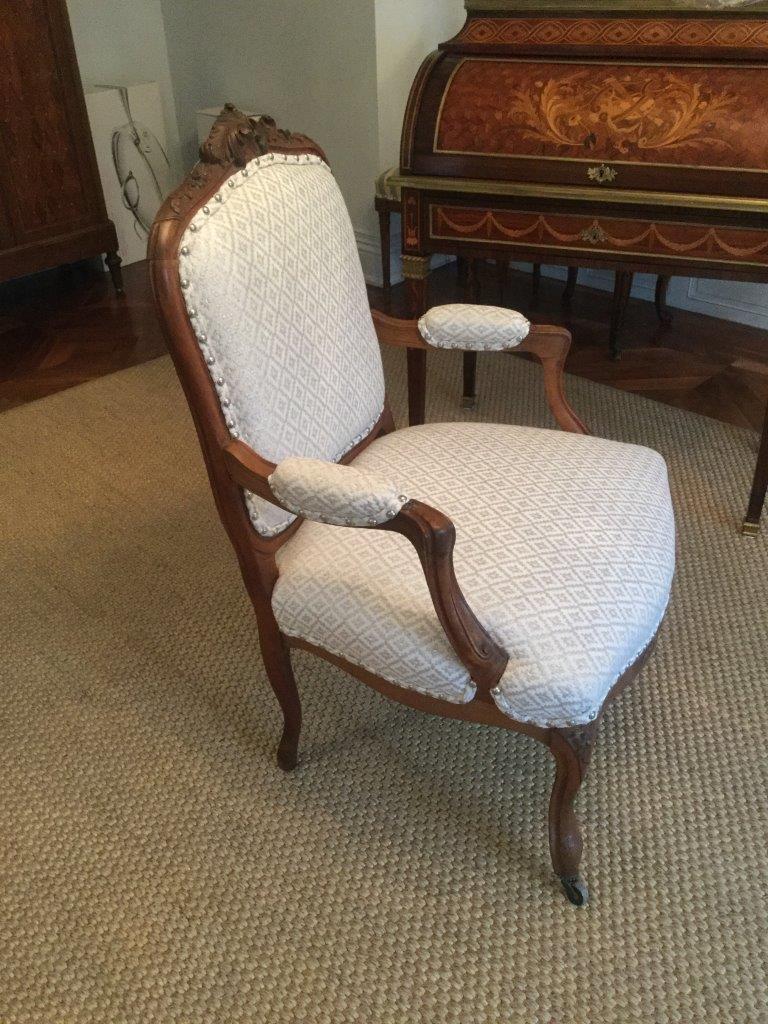 Stunning pair of carved walnut 19th century French arm chairs having beautifully carved frames with floral motifs at the crest and on the legs. The designer upholstery is a white on white diamond pattern. There are silver nailheads and same fabric