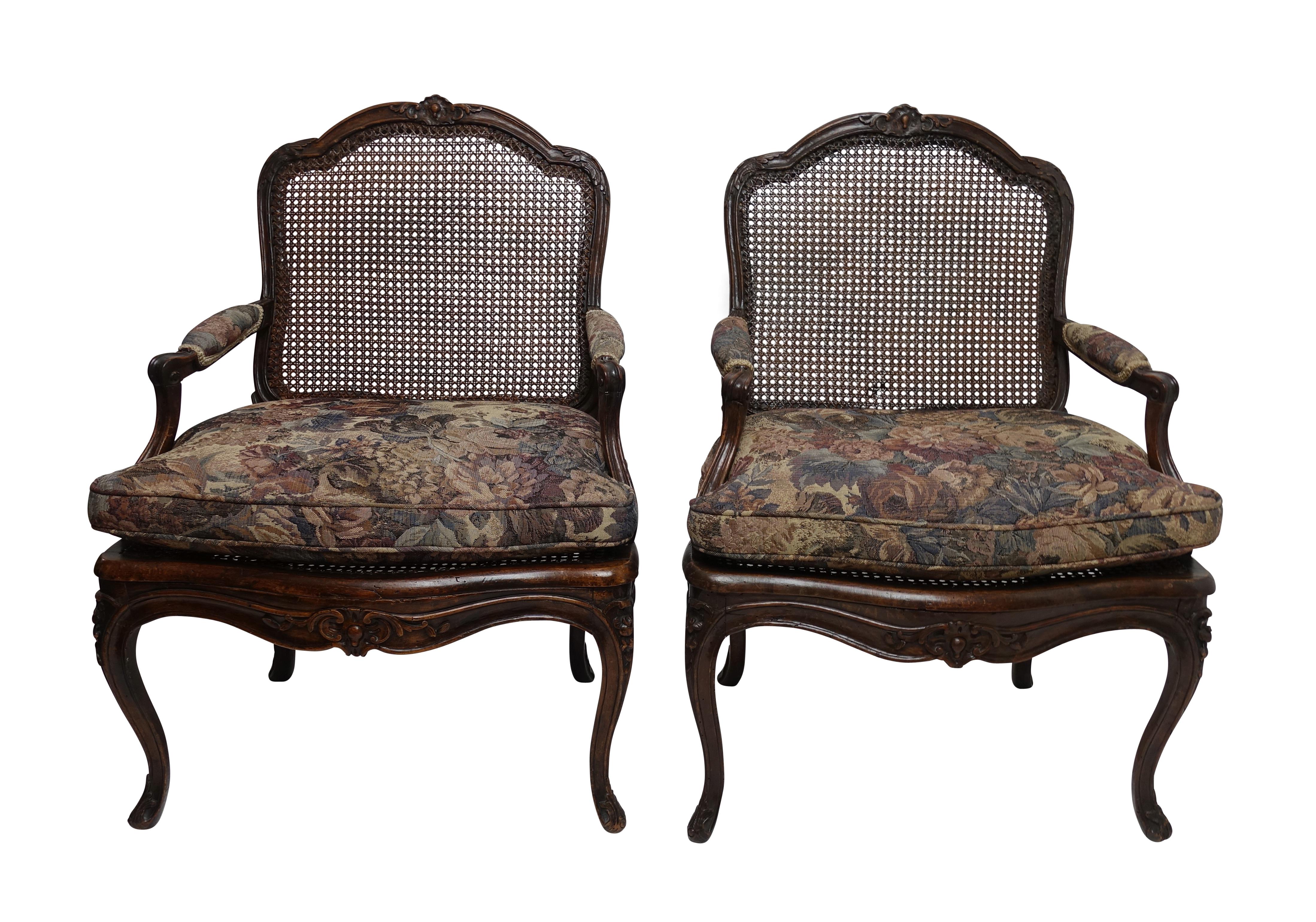 Pair of finely carved Regence Fauteuils with hand caned backrests and seats and vintage tapestry style upholstered fitted cushion. The frame of the chairs carved with acanthus leaves and the shaped crest rail centred with a shell carving as is the