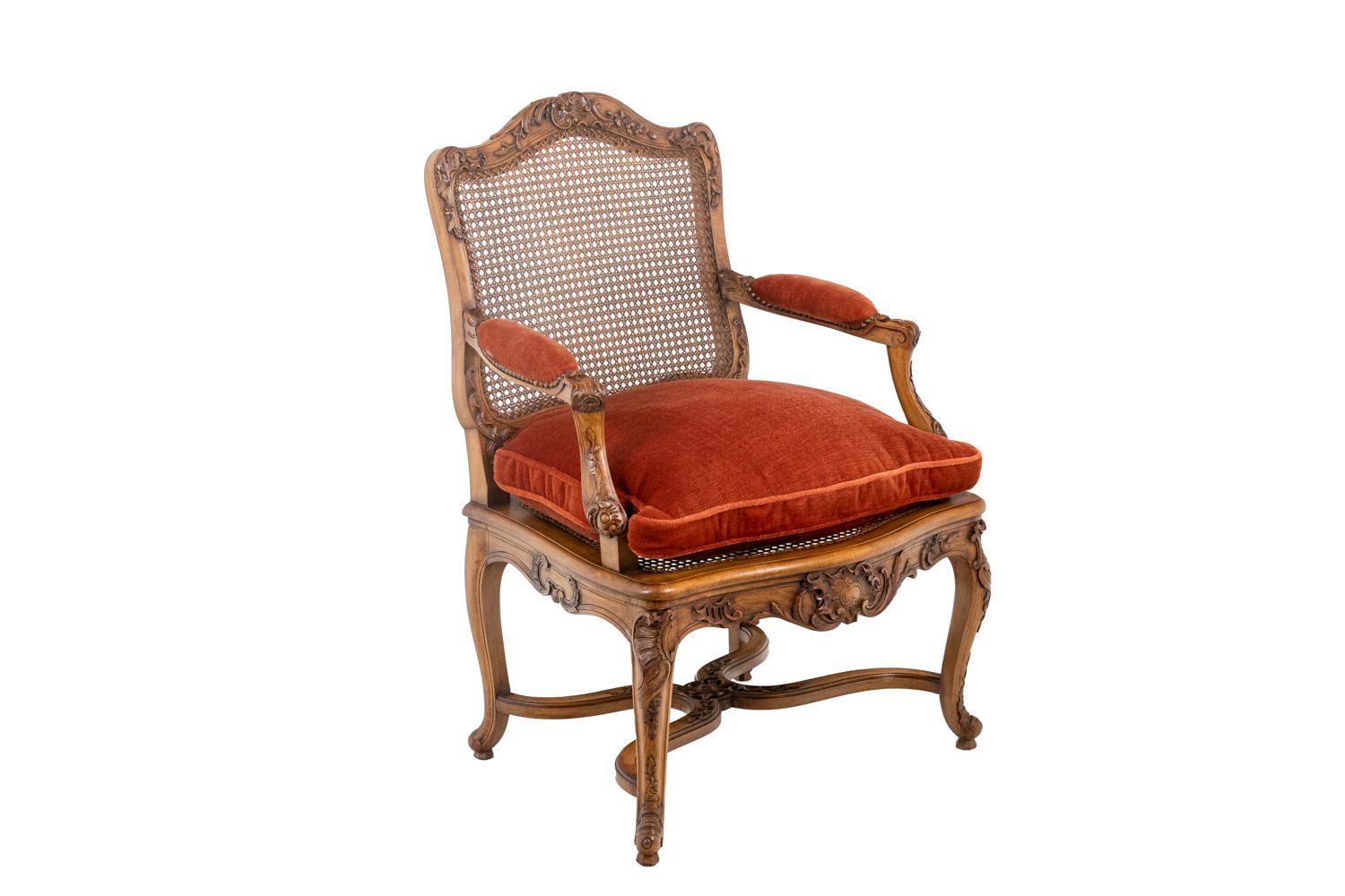 Ean Mocqué, stamp.
Louis Cresson, in the style of. 
Pair of Regency style armchairs in beech. Cane back and seat. Backrest and belt adorned with flowers, foliage and shells. Armrests consoles set back from the line of the foot. Arched feet joined
