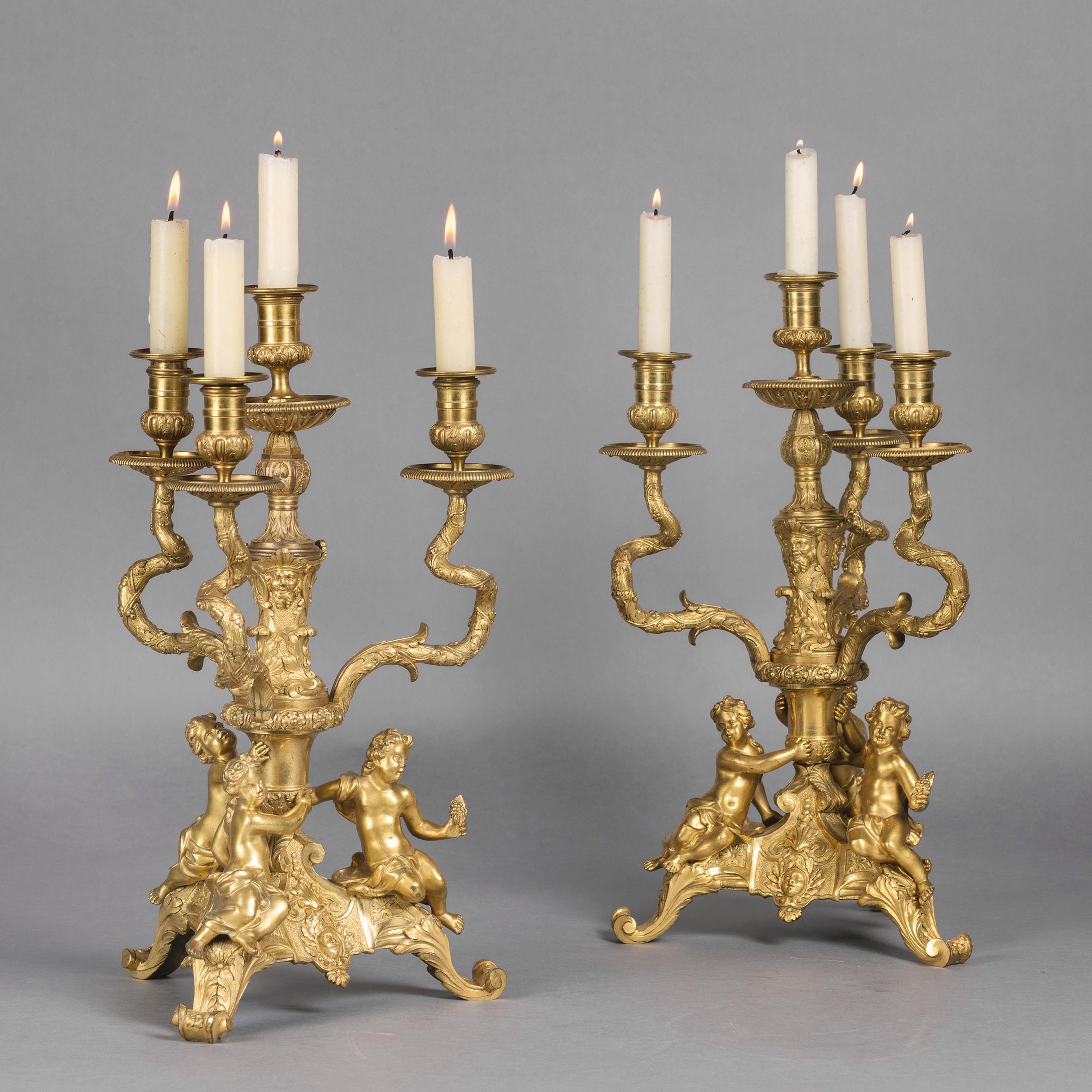 A fine pair of Regence style gilt-bronze figural four-light candelabra.

Stamped to the underside 'JB'.

Each candelabra has a tripartite base with putti figures supporting a central stem cast with grotesque masks issuing three acanthus and vine