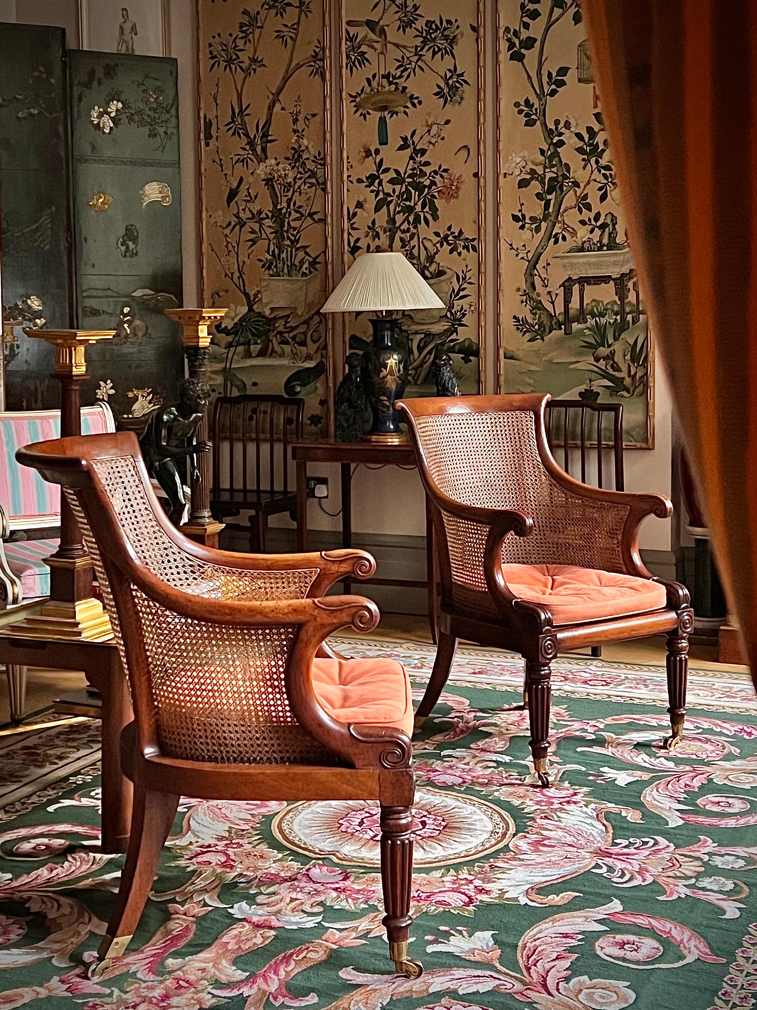 A pair of Regency bergère library armchairs, in the style of Gillows of Lancaster and London. With salmon faux suede buttonned squab cushions.
One chair English, circa 1825, the other one made to match at a later date, however, both chairs acquired