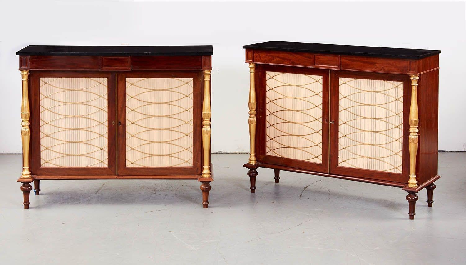 Good pair of Regency cabinets, the black painted tops over mahogany and giltwood cabinets with two drawers over two brass grill work doors flanked by turned giltwood columns and standing on gilt turned legs.