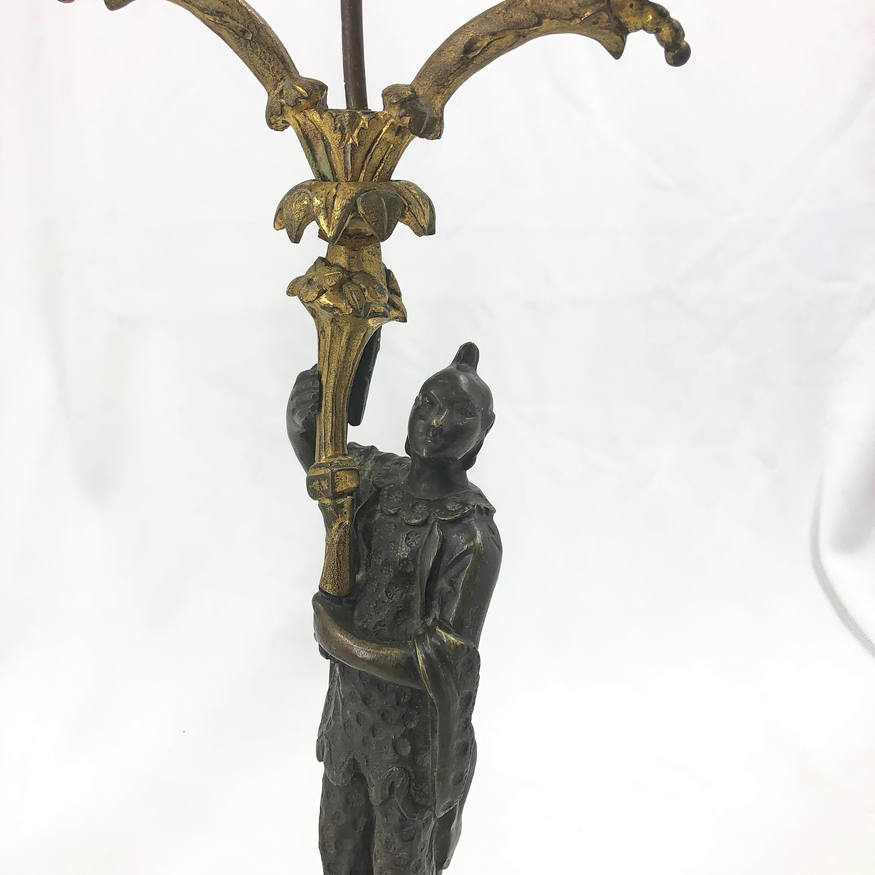 A rare pair of Regency chinoiserie figural candelabra with traditionally dressed men in robes holding a gilt bronze palm tree and leaf form arms, standing on bronze chased round neoclassic pedestals.