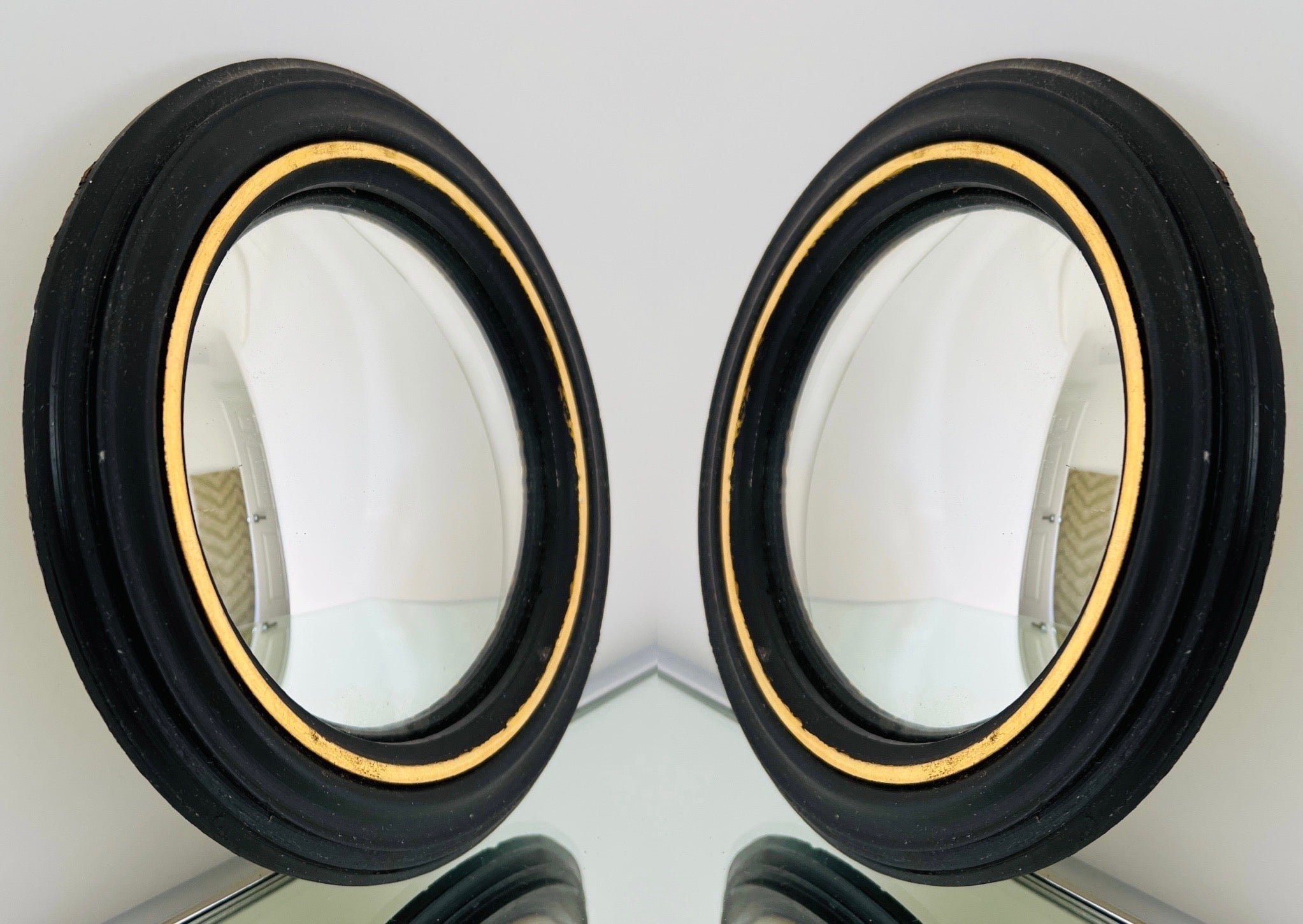 English Regency style small convex mirrors with round molded plaster frames.  Hand-carved design featuring fluted rims, with ebony finish and distressed gold leaf accent.  Used throughout centuries, bullseye mirrors add an architectural element to a