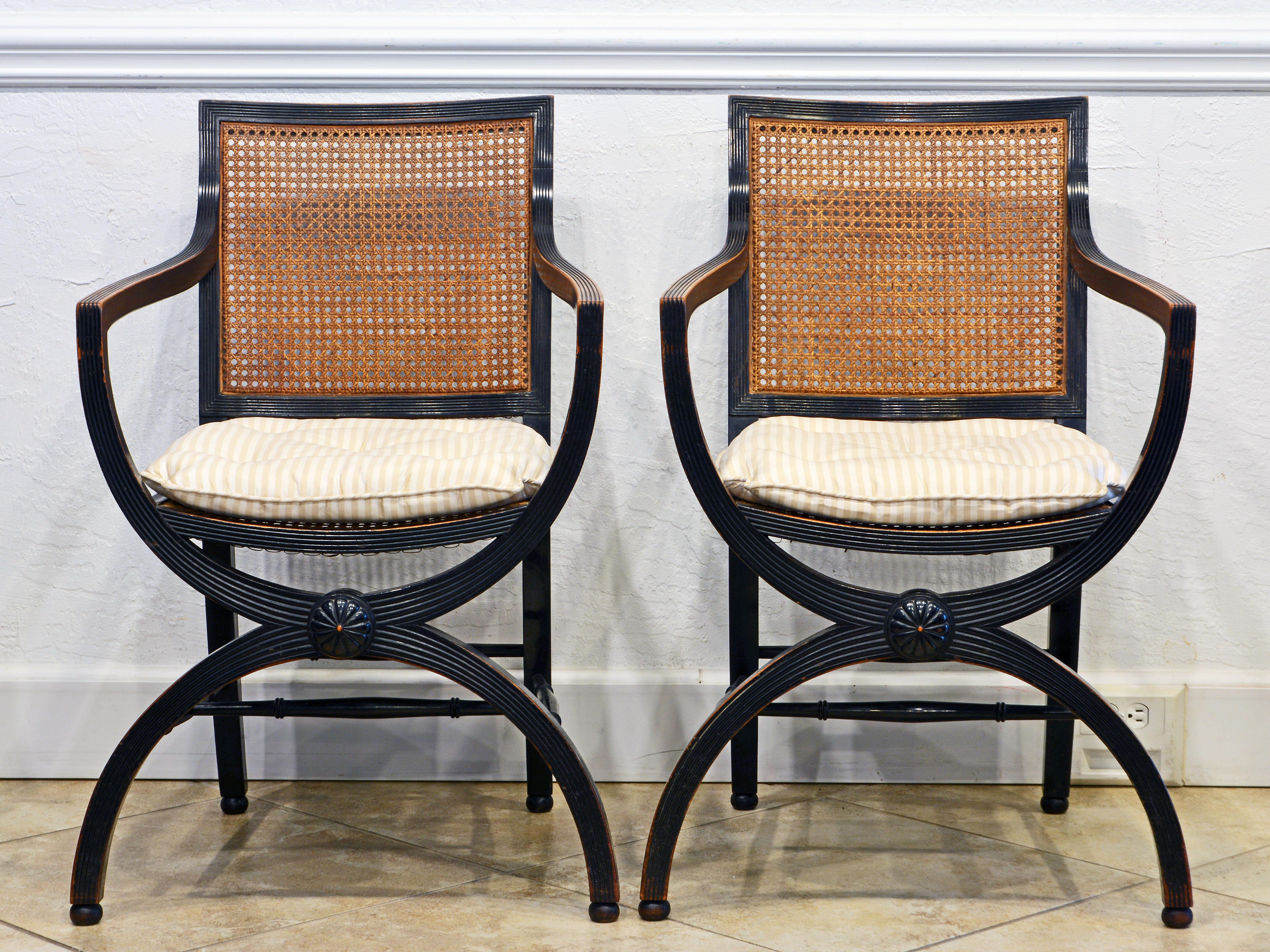 This distinguished pair of Regency armchairs in the manner of Thomas Hope feature elegant reeded and ebonized frames inspired by the classical curule type of legs. Seats and backrests are traditionally caned and later supplied with tasteful