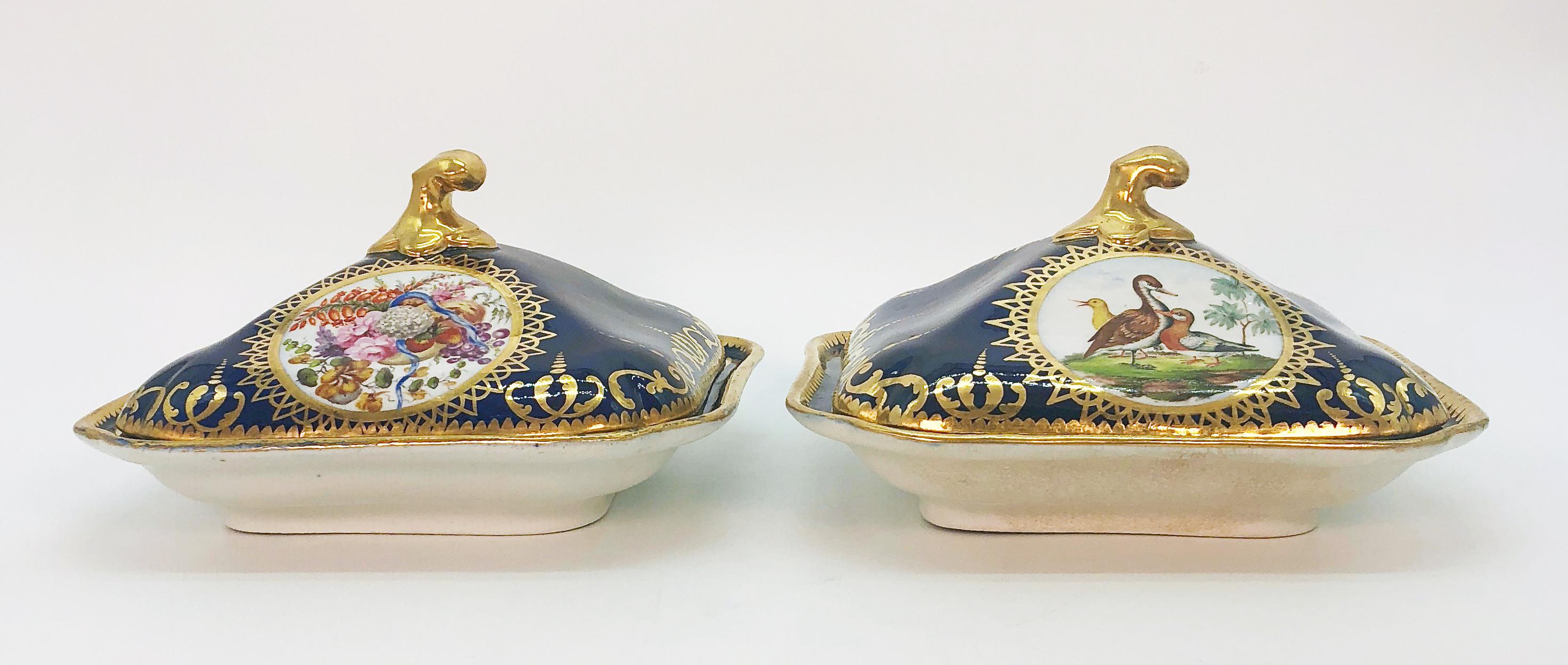 A pair of Coalport cobalt blue square covered vegetable serving dishes decorated with gilded bands of interlocking scrolls and finials. Hand painted panels to dishes and lids, one decorated with waterfowl and game birds and the other with floral