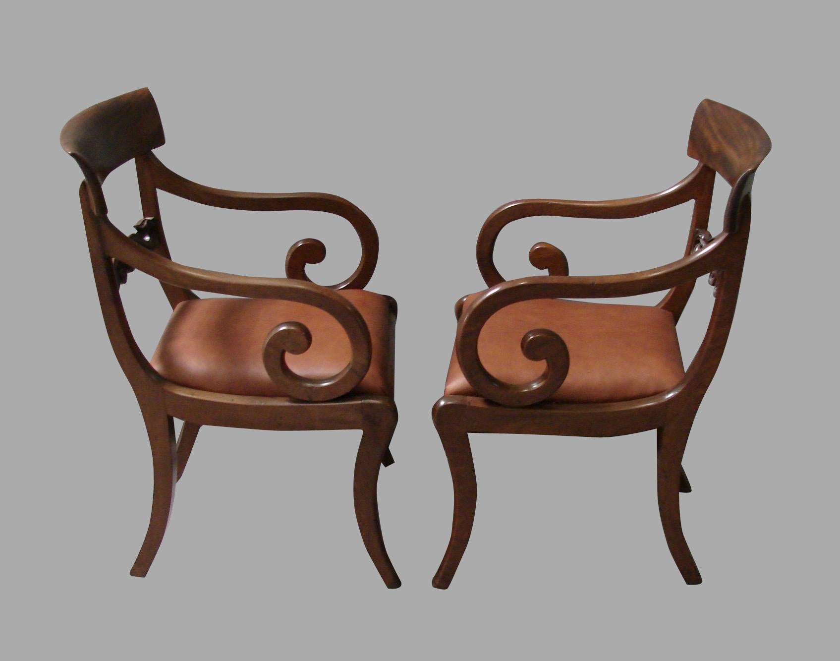 A pair of good scale Regency mahogany armchairs with scroll arms and newly upholstered drop in leather seats supported on saber legs. Each with a carved horizontal back splat. These chairs sit well. Circa 1825-1830.