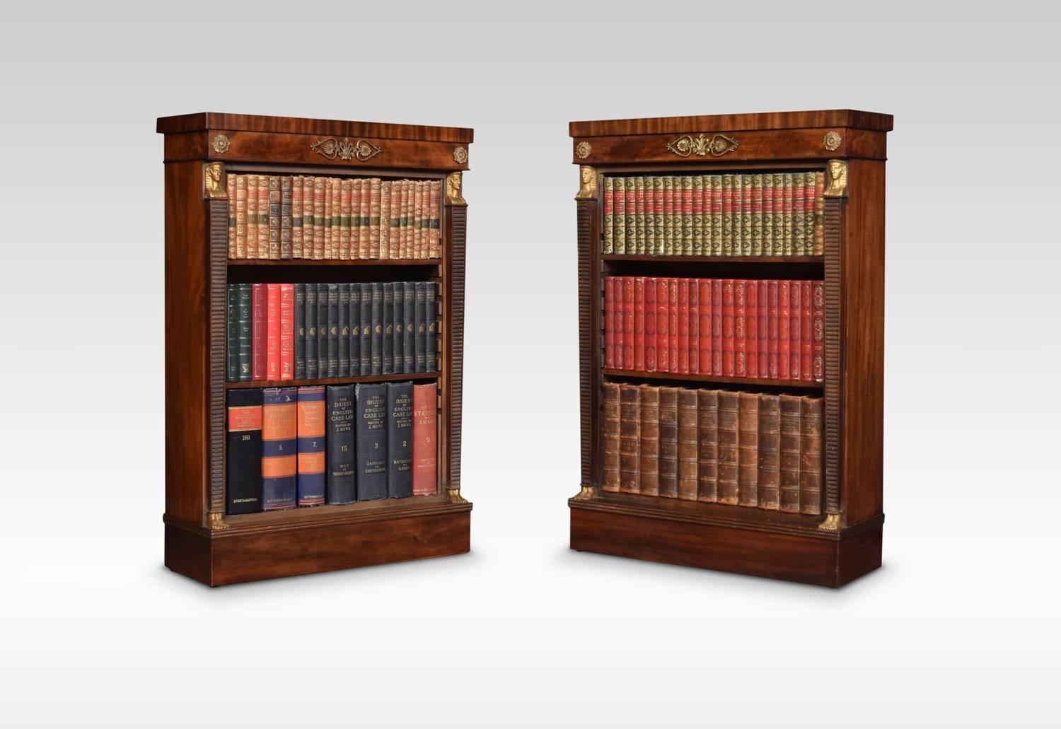 A pair of Regency style mahogany open bookcases. The rectangular tops above gilded mounted freezes to the open shelves fitted with two adjustable shelves in each section, flanked by Egyptian influence columns. All raised up on plinth