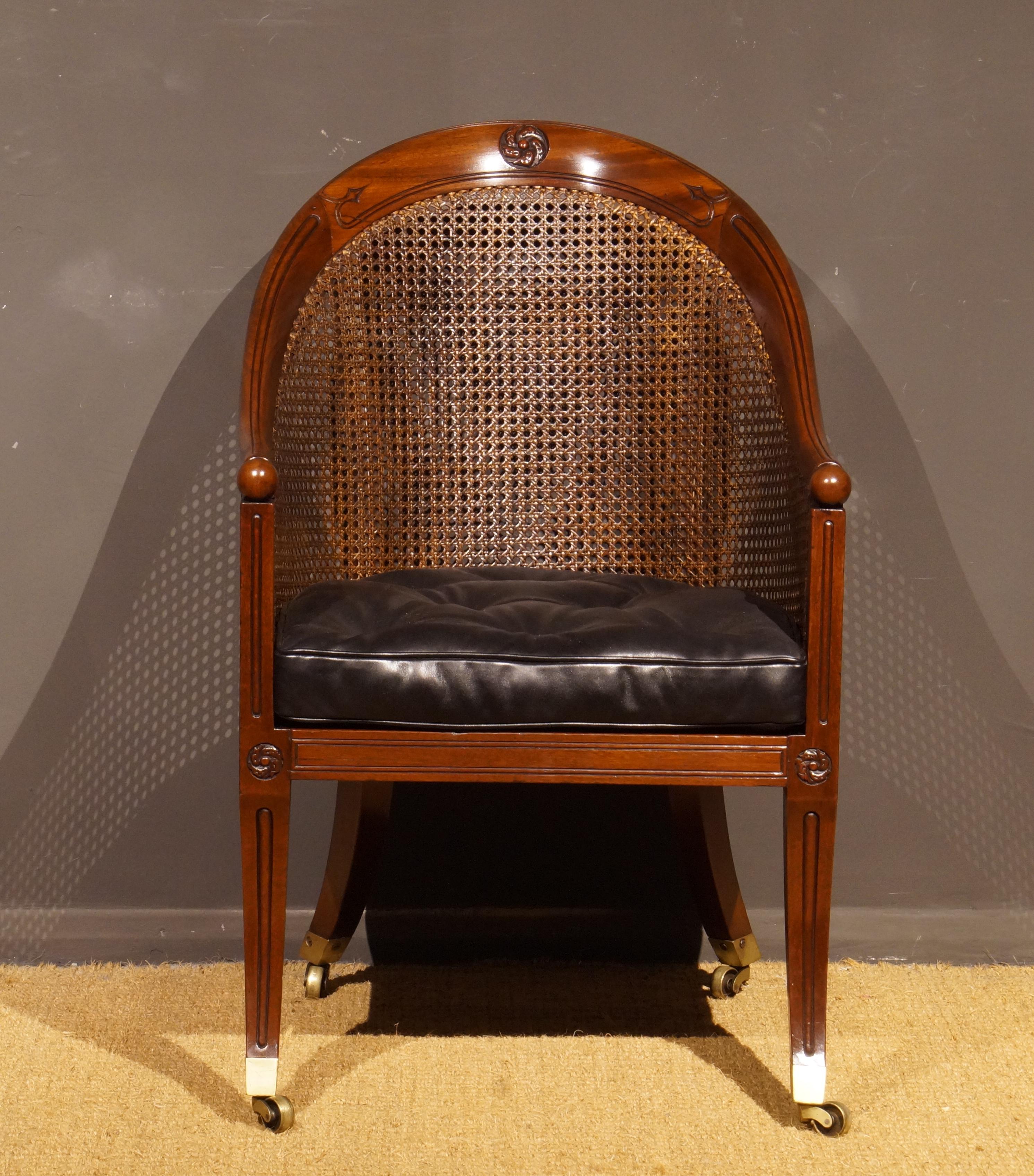 A fine pair of chairs, the curved backs and arms with carved decoration and ball ends, supported by moulded uprights and sabre legs front and back terminating in brass cap castors; the caned seats with recently covered black leather squab
