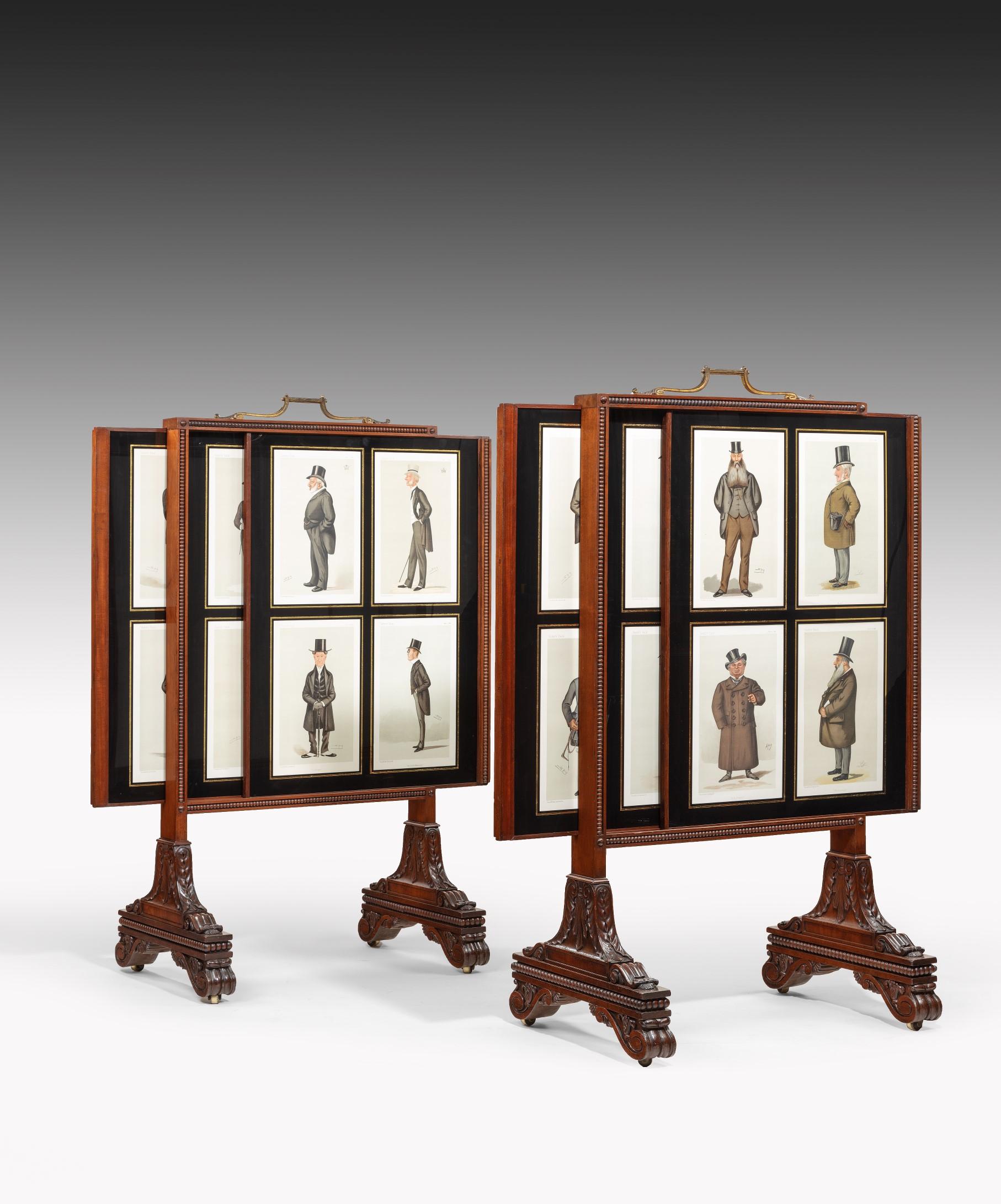 A fine pair of Regency period carved mahogany fire screens displaying a set of vanity fair spy cartoons of top hatted gentlemen; the screens retaining their original scrolling ormolu handles above a mahogany frame carved with coing mouldings with