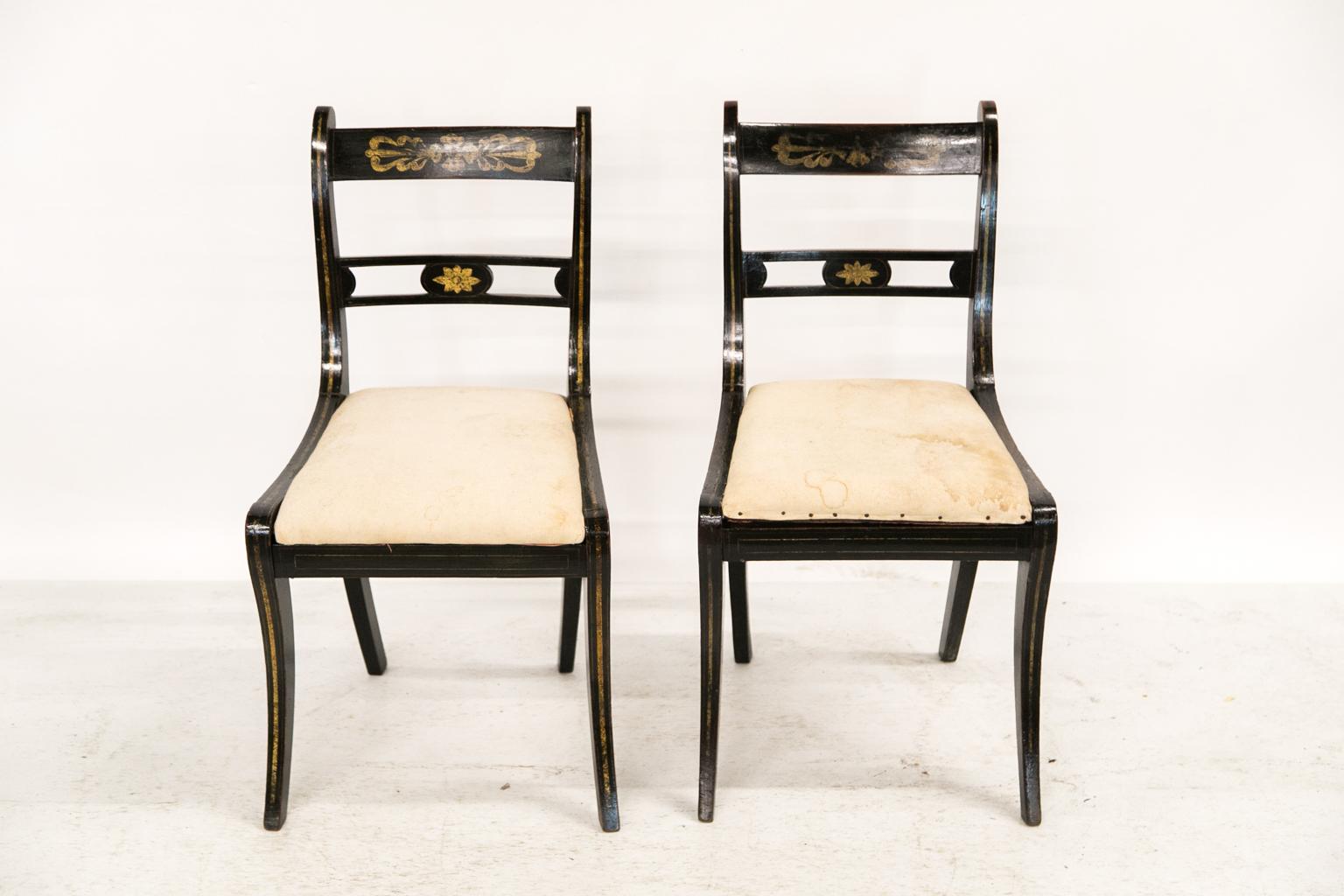 This pair of Regency side chairs has a pierced center cross splat with a floral starburst medallion in the center. The back stiles, seat frames, and front legs have a sweeping gold 1/4