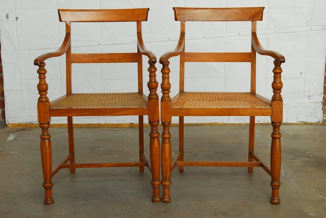 Elegant pair of Regency style Anglo-Indian colonial armchairs featuring caned seats. Beautifully constructed from hand-carved mahogany with turned front legs and arm supports. Delicate style that showcases the lovely grain of the wood.
