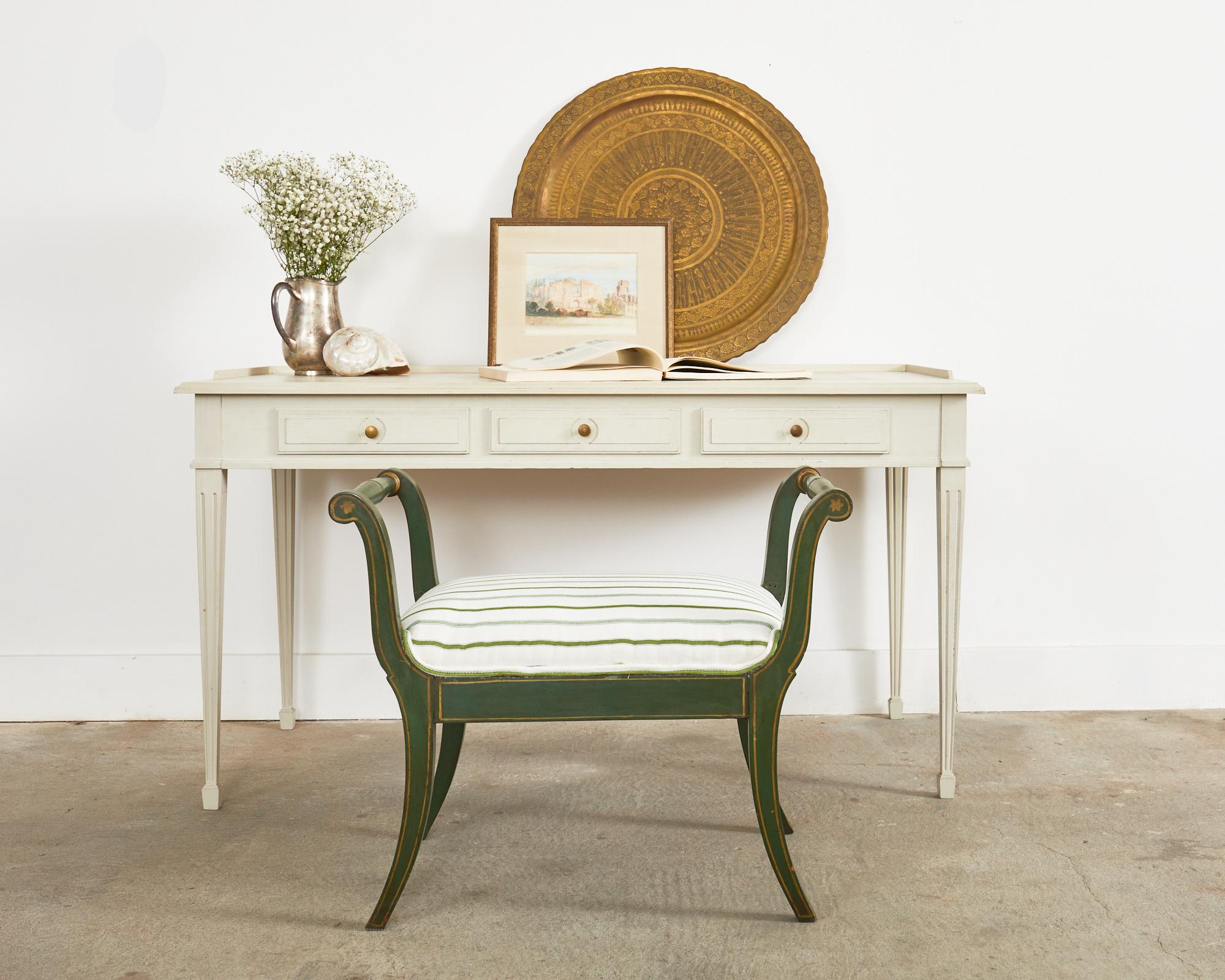 Extraordinary pair of lacquered olive green benches or stools made in the regency taste. The stools feature a gracefully splayed klismos style legs with delicate parcel gilt accents. The newly upholstered seat is topped with a playful green, white,
