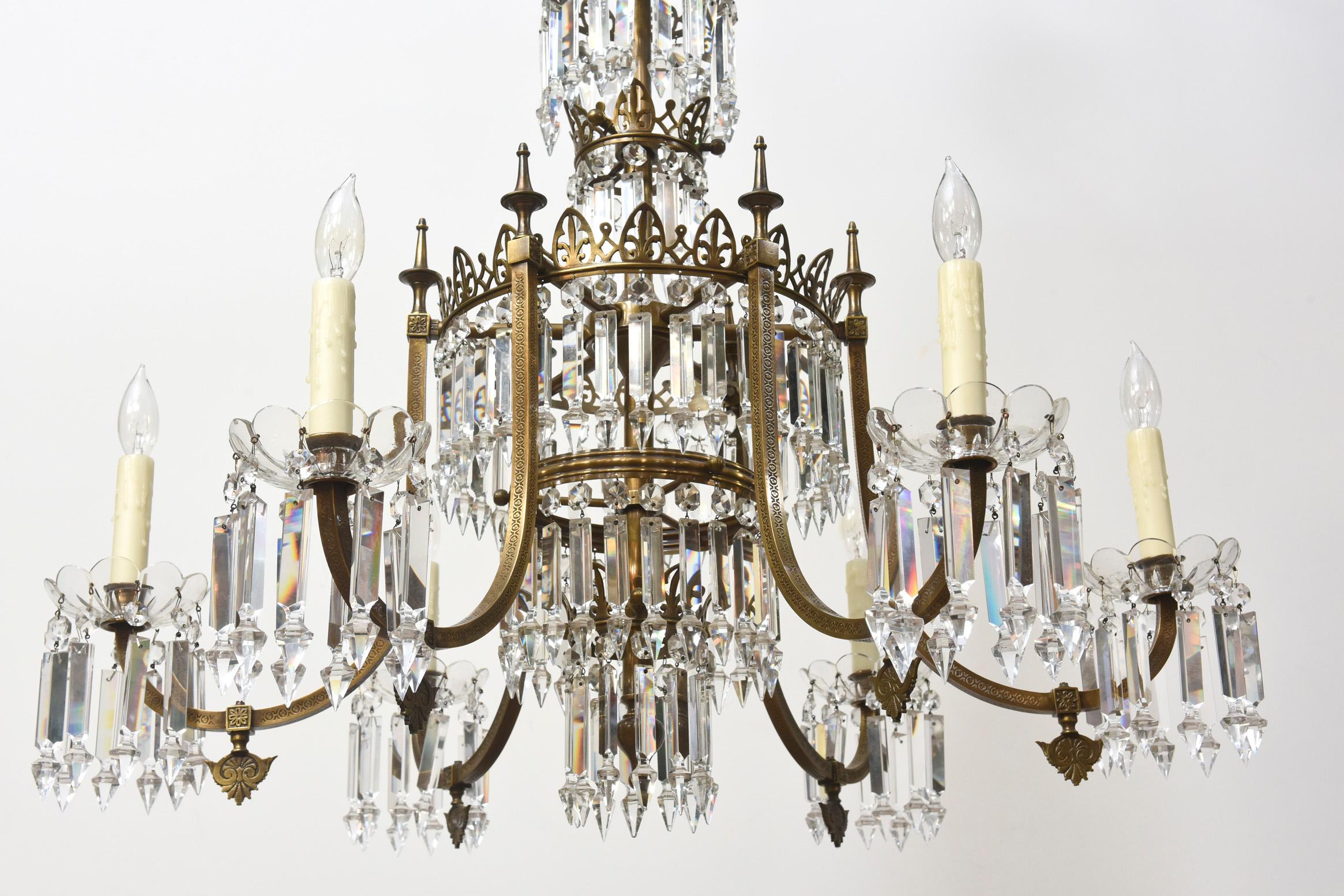 Pair of six arm brass and crystal chandeliers. Six tiers of crystals around the central stem. Stamped brass square tubing on arms topped with urns. Crown details on each ring. Original Chandeliers from a property on Lewisburg Square, Boston.
