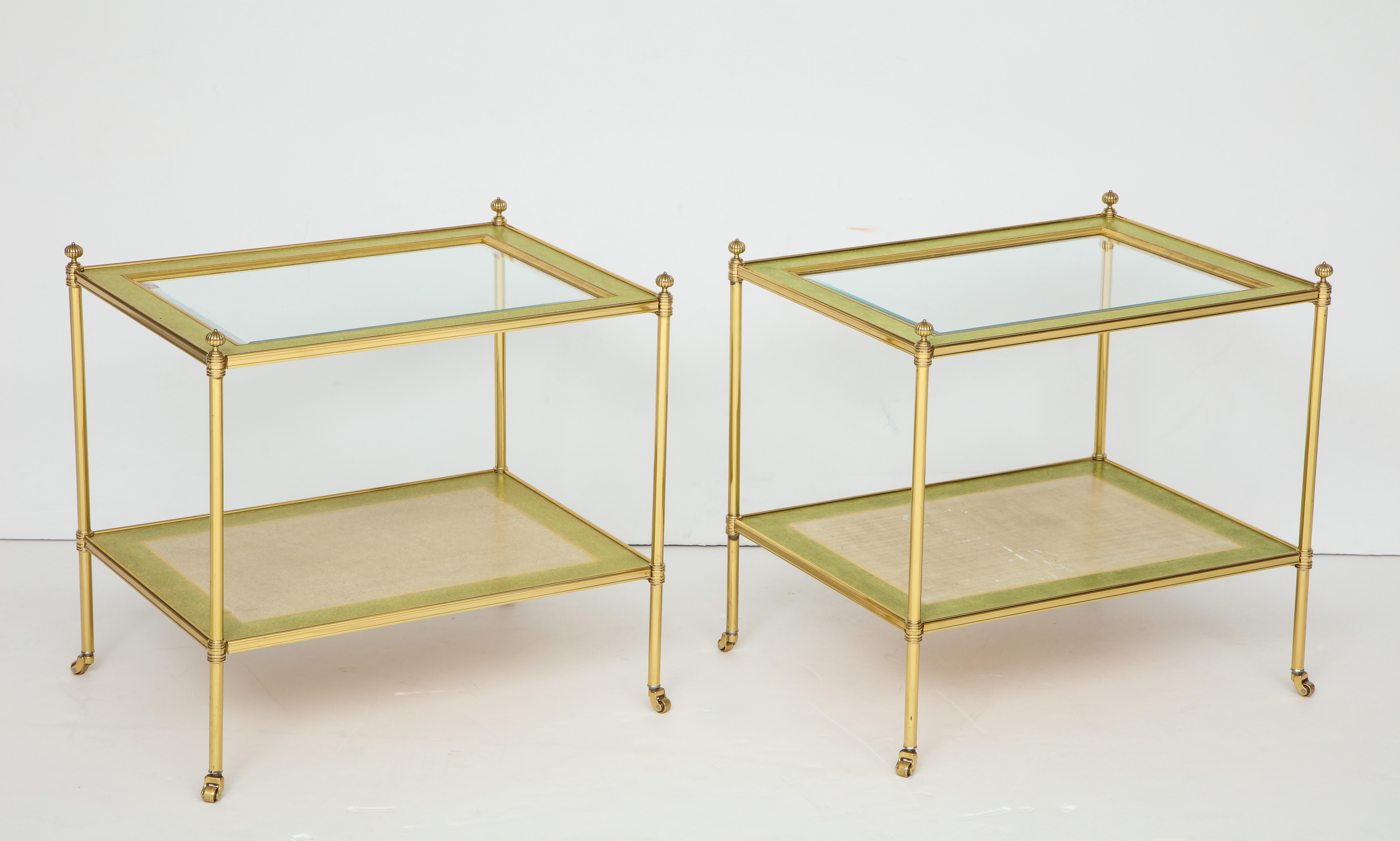Each with four brass rods, topped with a molded finial and resting on brass rollers, all supporting two shelves: each with a faux painted brass frame and inset with glass.