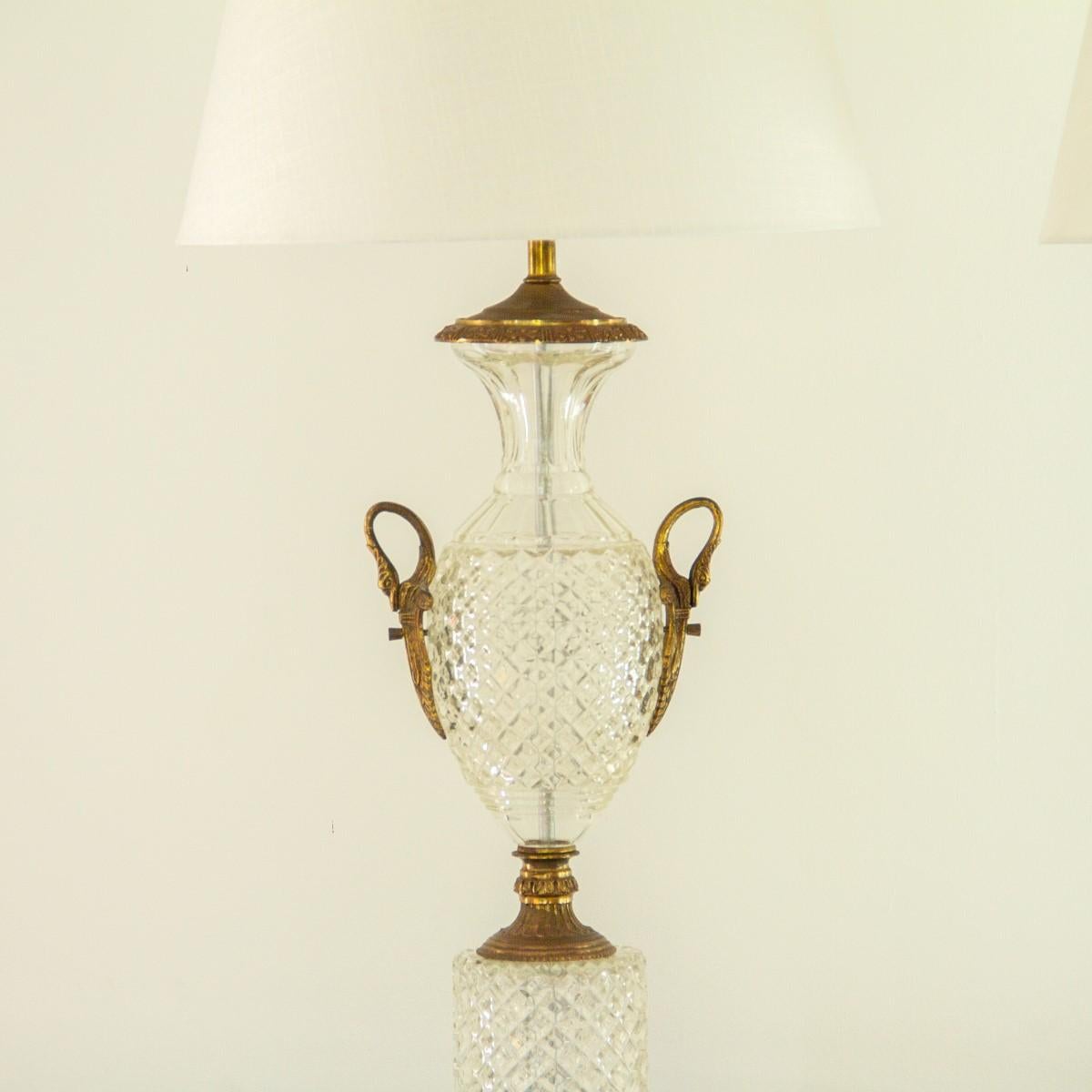 A pair of Regency style cut crystal, amphora urn shaped lamps with antique brass handles depicting swans and brass details to the socle, rim and base. The lamps are set on veined marble bases, circa 1960s.

Good condition

Currently on display