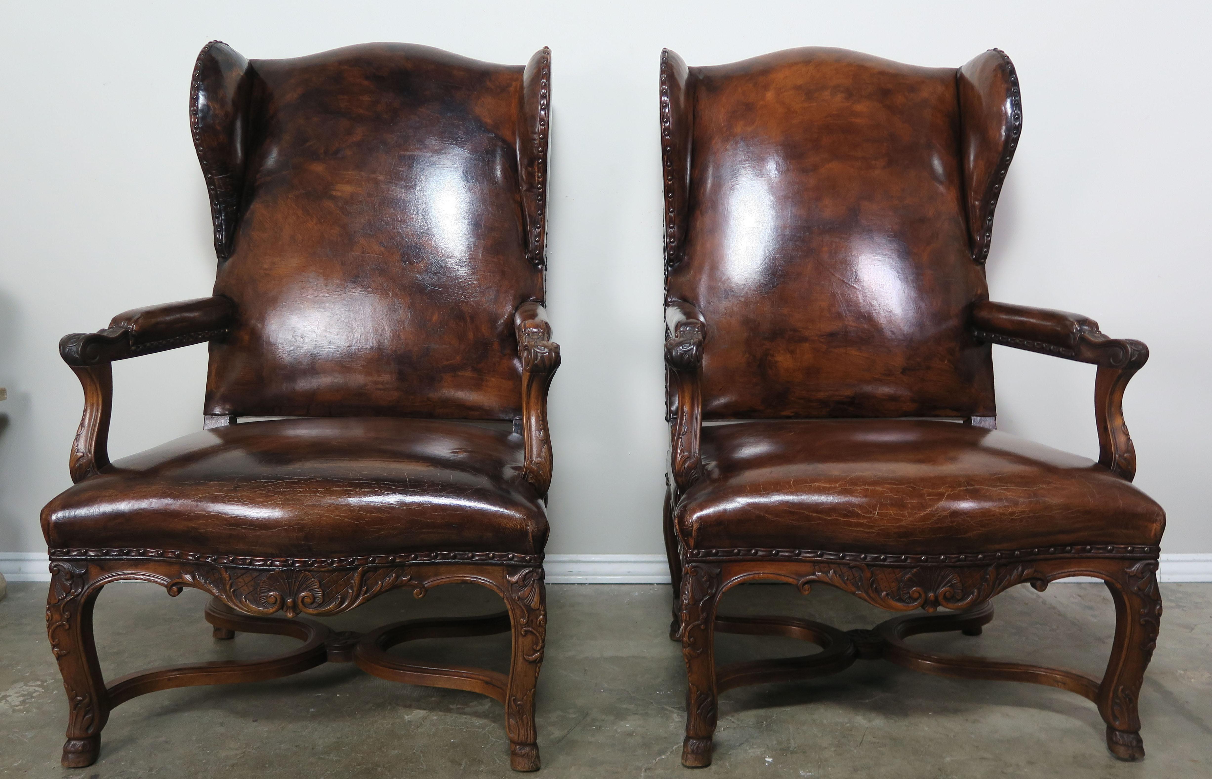 Pair of handsome Regency style rich leather upholstered French wing-back armchairs with nailhead trim over flat welt detail. The chairs stand on four cabriole legs that meet at centre 
