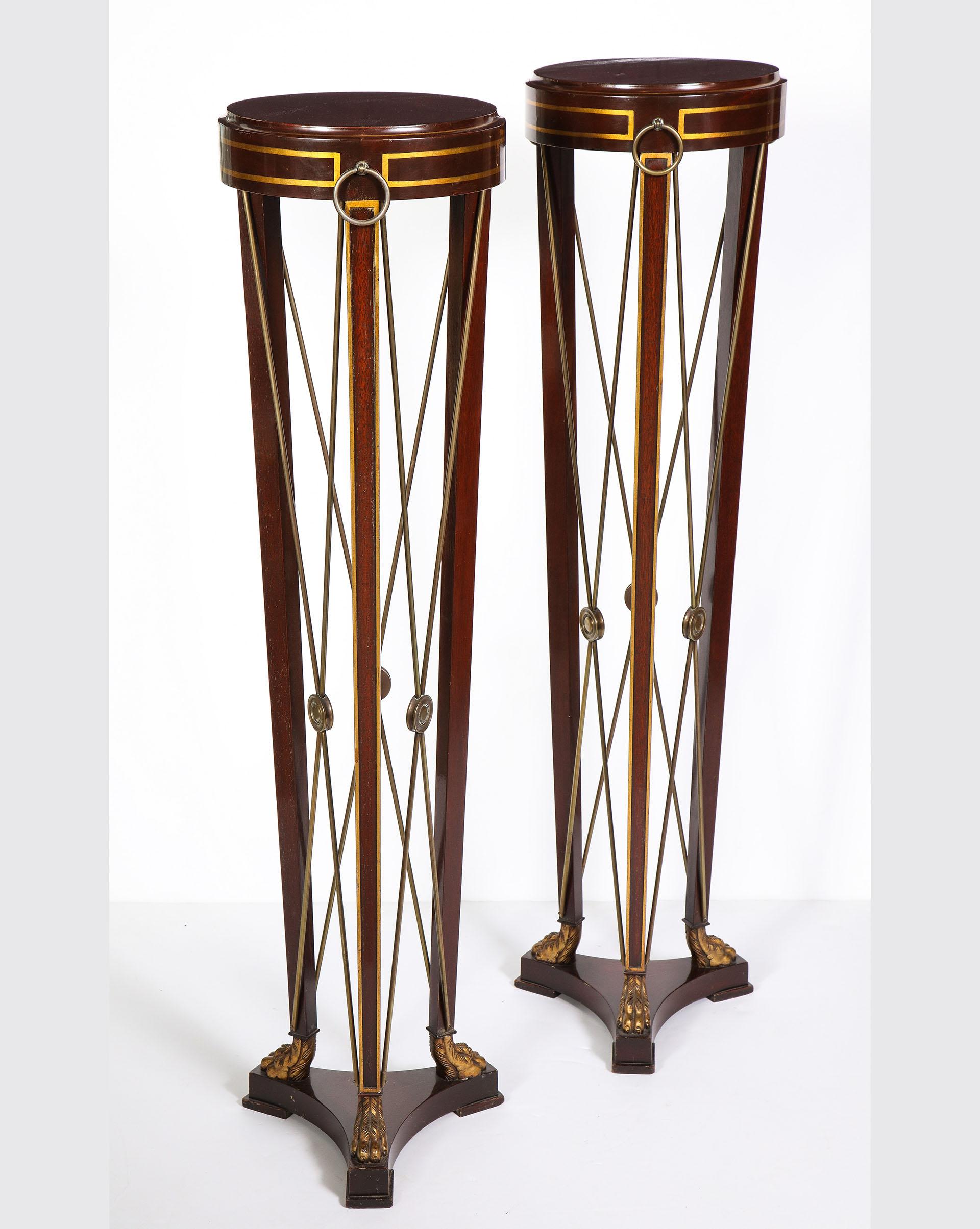 Each mahogany pedestal with pencil line gilded detailing and a brass cross support with gilded claw feet on a triparte base.