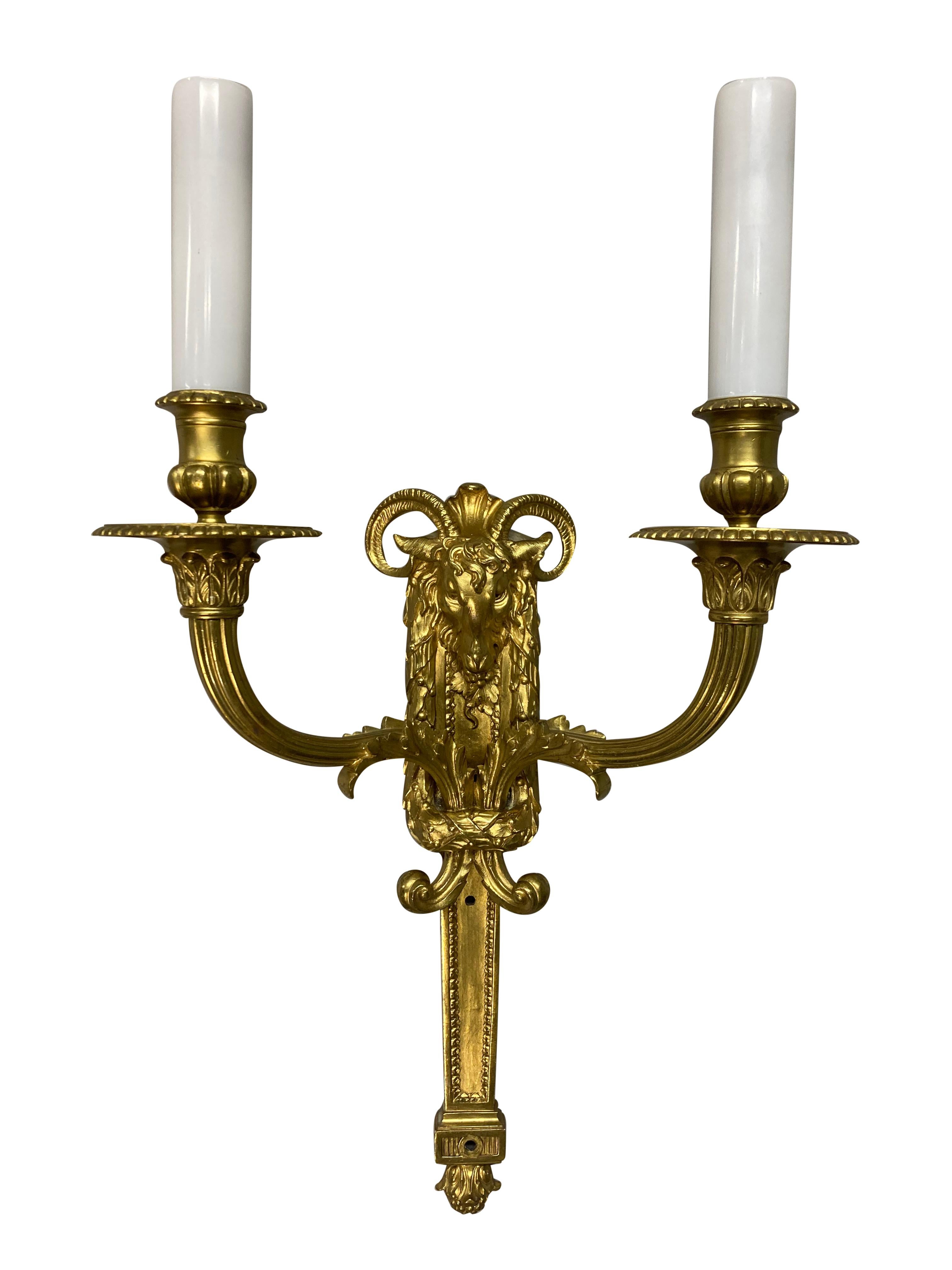 A pair of English gilt bronze Regency style twin branch wall lights. Of good quality, with rams heads and acanthus decoration. With white glass sleeves.