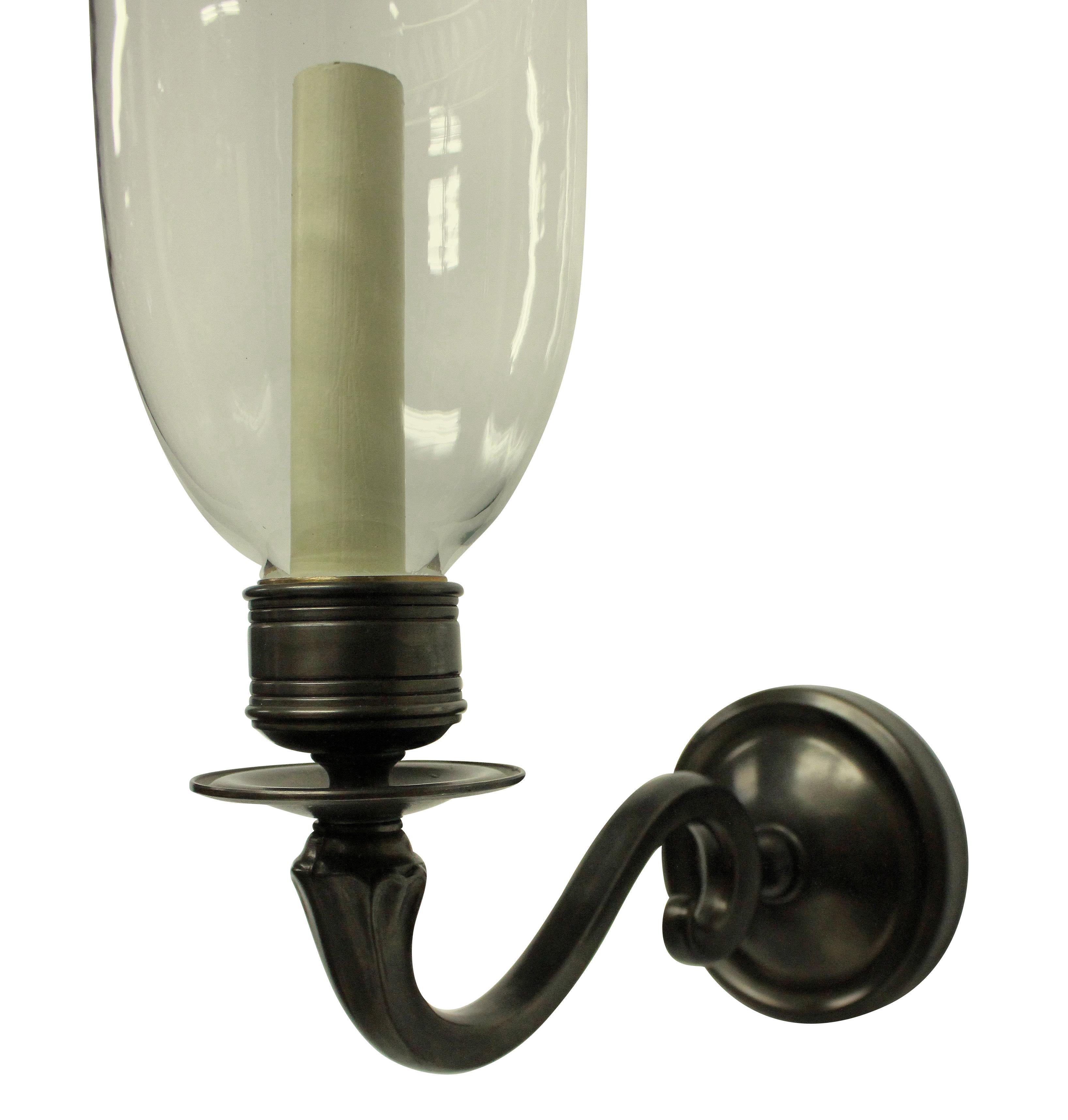 A pair of English Regency style bronzed wall lights with glass storm shades.