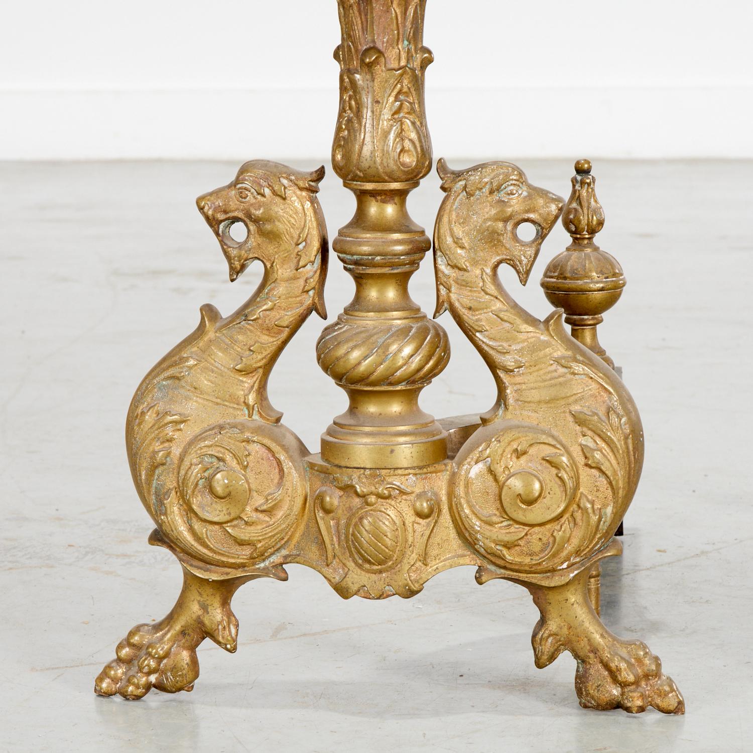 An elaborate pair of Renaissance Revival chenets or andirons in gilt brass, each featuring opposing dragon-form supports surmounted by a baluster stem with acanthus ornamentation, terminating in a polished onyx sphere and foliate finial. The design