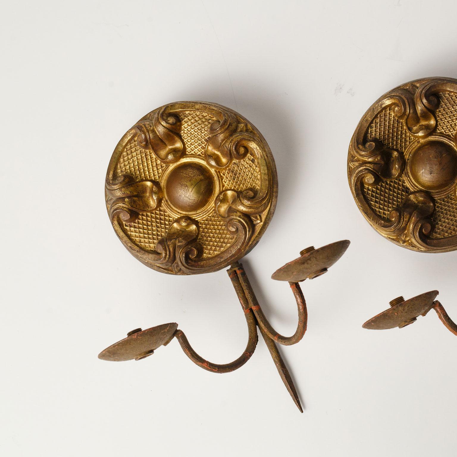 Pair of repousse sconces with two iron arms each. Remnants of gilt decorate surface of the brass repousse. Dating to the mid-late 19th century. Unwired, but can be wired for electricity for an additional cost. Sold together as a pair for $850.