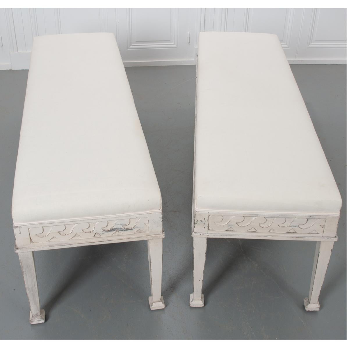 This fantastic pair of painted reproduction benches, features upholstered cushions resting upon an apron with a Vitruvian scroll design. The whole is raised on six tapered legs with shaped feet.