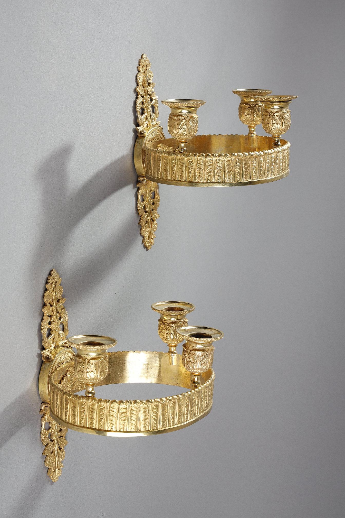Elegant pair of wall sconces in finely chased and gilded bronze, typical of the refined taste of the Restoration period. Each sconce features a circular structure decorated on the outside with a frieze of palmettes and on the inside with a floral
