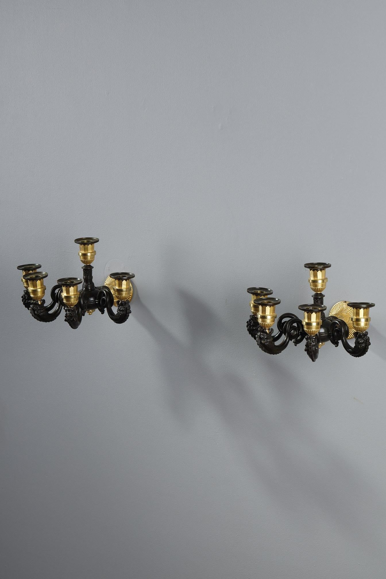 Pair of restoration period sconces with five light arms on two levels in gilt bronze and patina. The wall part is decorated with palmettes and scales motifs leading to a circular connection from which the light arms radiate. The upper right jamb is