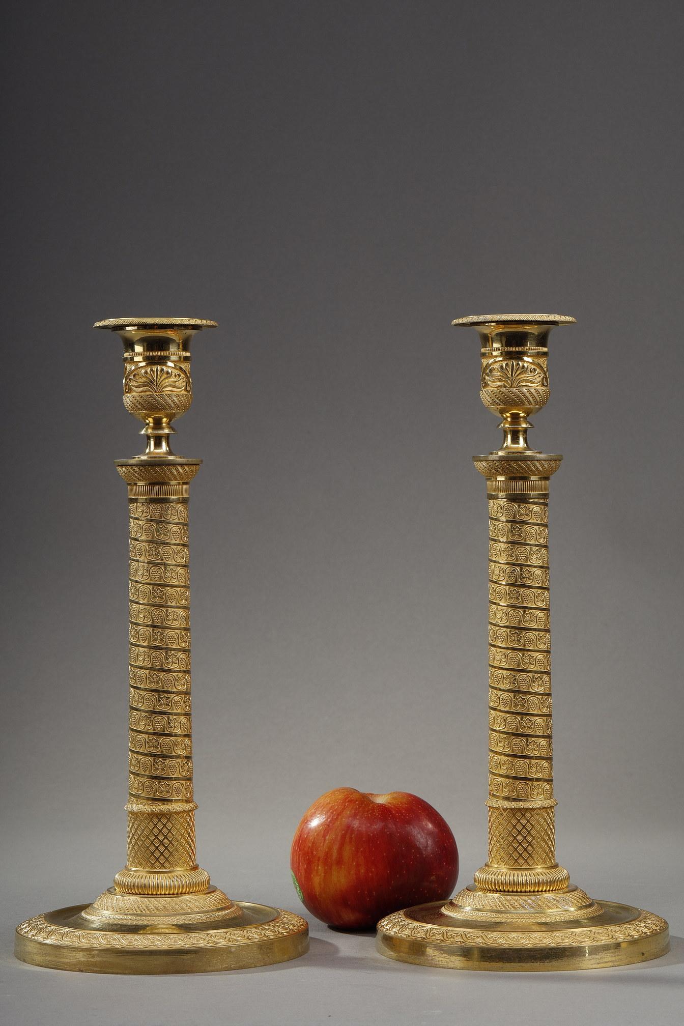 Pair of candlesticks from the Restoration period in chased and gilded bronze with a shaft in the shape of columns whose decoration of vine bulbs scrolls around in a spiral. The circular base is decorated with a crown of laurels, interlacings and