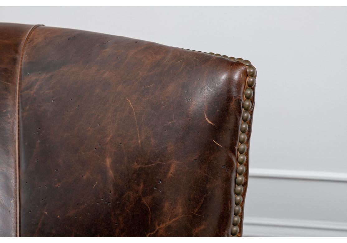 Pair of restoration hardware drake leather barrel back club chairs modeled after traditional English Style fireside chairs featuring kiln-dried hardwood frame with a curved back and deep wings with Whiskey Brown leather, antique brass nailhead trim