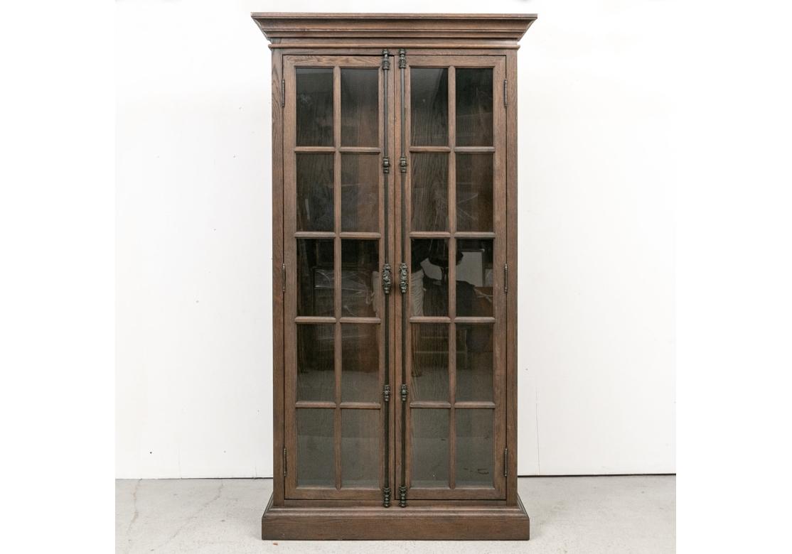A pair of very well made, sturdy and solid feeling Display/ Bookcase Cabinets in an oak drift wood type finish The Cabinets with crown molding over double glazed doors with French style intricate cast metal hardware with knob handles. With four wood