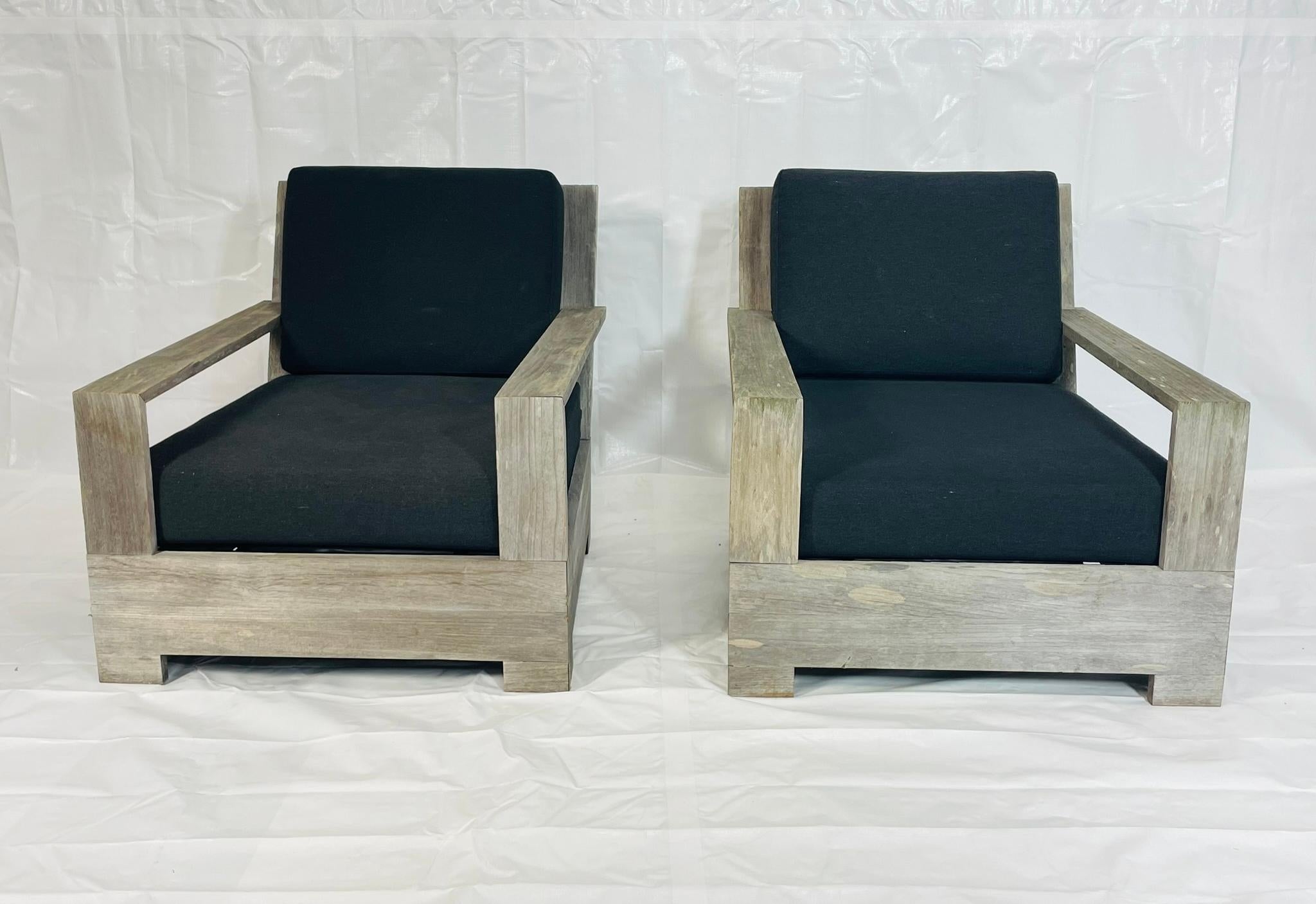 Una coppia di poltrone da patio in teak massiccio di Restoration Hardware, progettate con linee architettoniche audaci e proporzioni generose che bilanciano il comfort con una durata senza tempo. Ogni sedia è caratterizzata da una robusta struttura