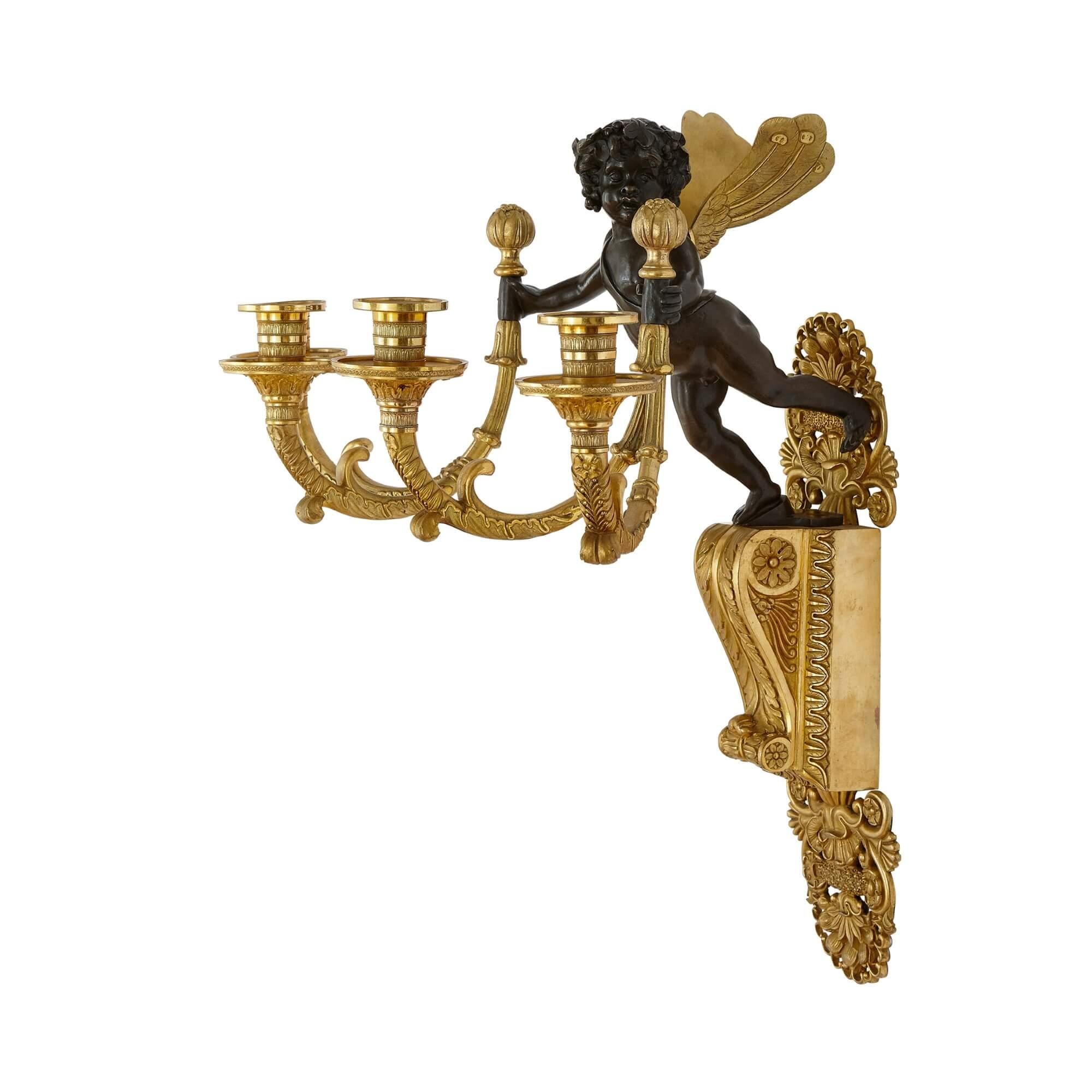 Dating from the Restauration period, these beautiful wall-lights combine a variety of stylistic influences to make a an exceptional pair of interior pieces. Each object features a winged putto descending from above, holding out a scrolling branch