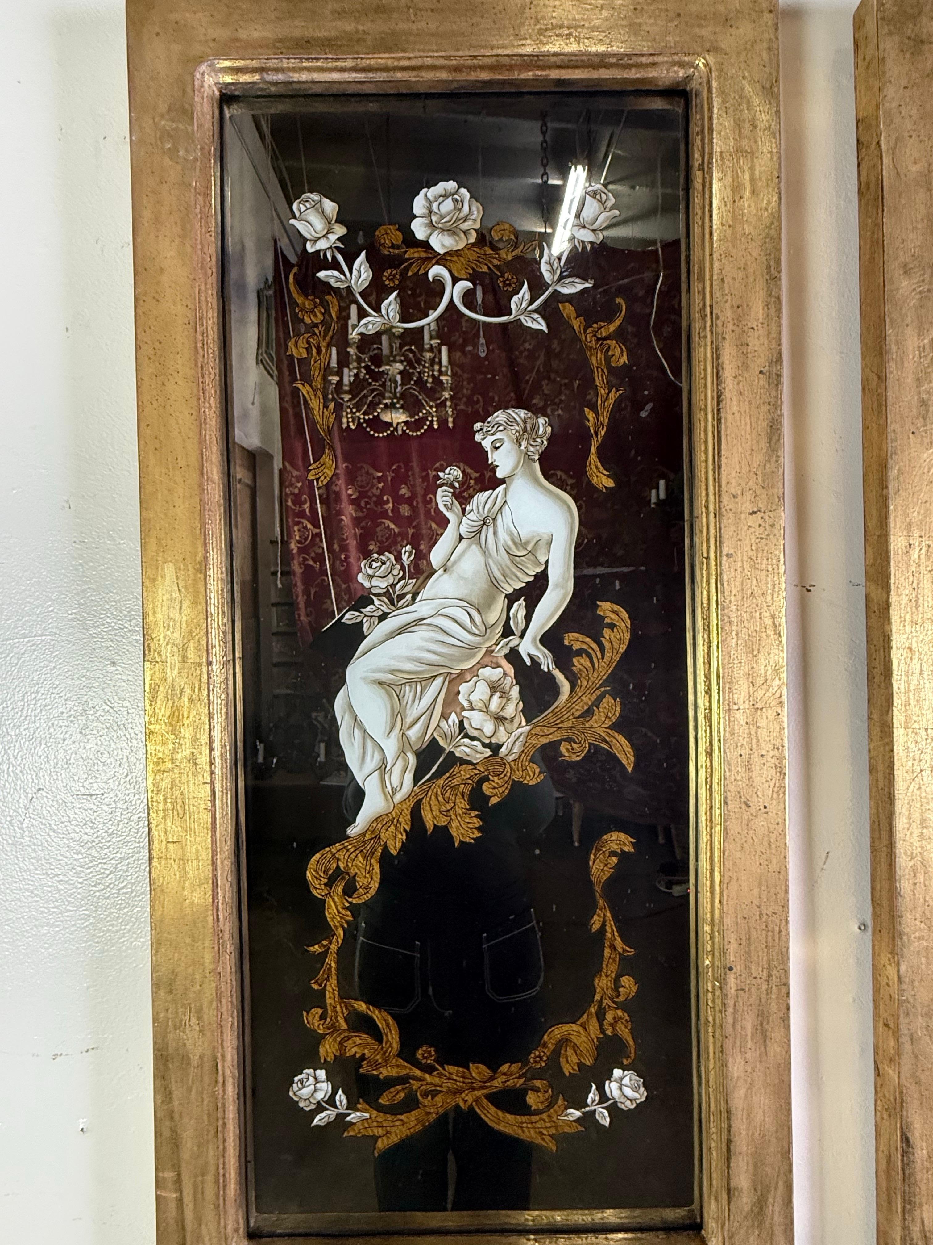 A refined pair of reverse-painted mirrored panels, exquisitely detailed with classical female figures draped in flowing robes. Each figure is surrounded by ornate gilt foliate scrollwork and delicate white roses, creating a sophisticated composition