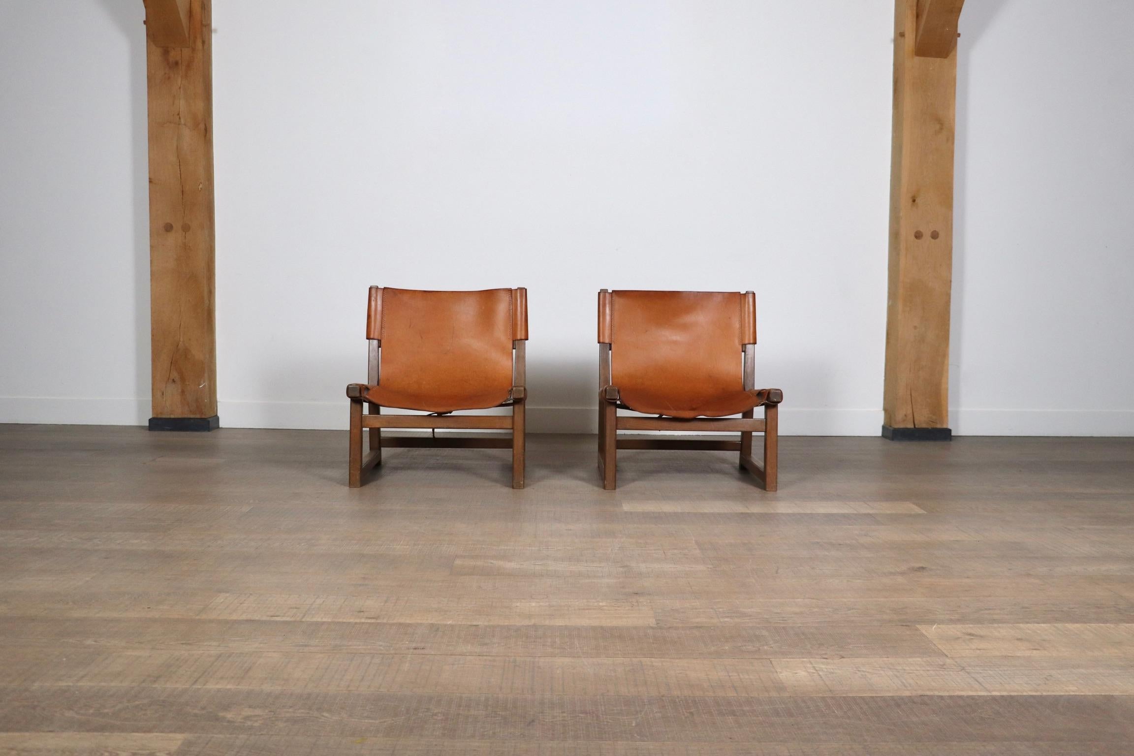 Fantastique paire de chaises Riaza en cuir cognac par Paco Muñoz pour Darro Gallery, Espagne, années 1960.
S'inspirant de l'esthétique des chaises de chasse, le revêtement en cuir cognac, vaguement attaché au cadre par des sangles, ajoute une touche