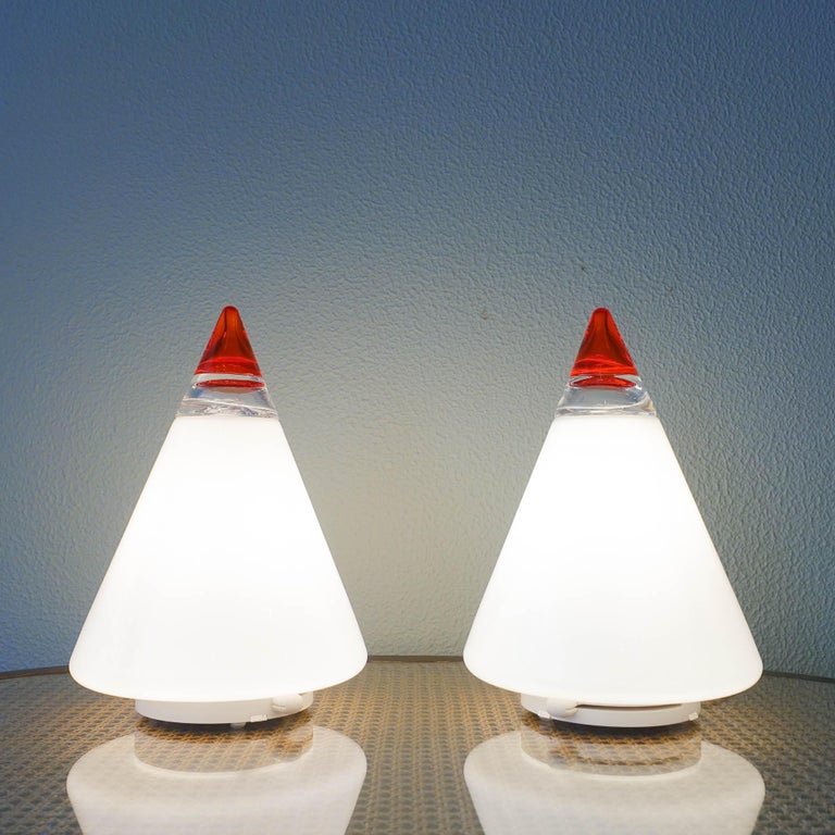 “Rio Grande” is the name of this pair of table lamps, product manufactured by Leucos and designed by Giusto Toso, in Italy, during the 1970's. It has a cone shape in white glass, with clear and red colored glass in the tip as a finish, supported by