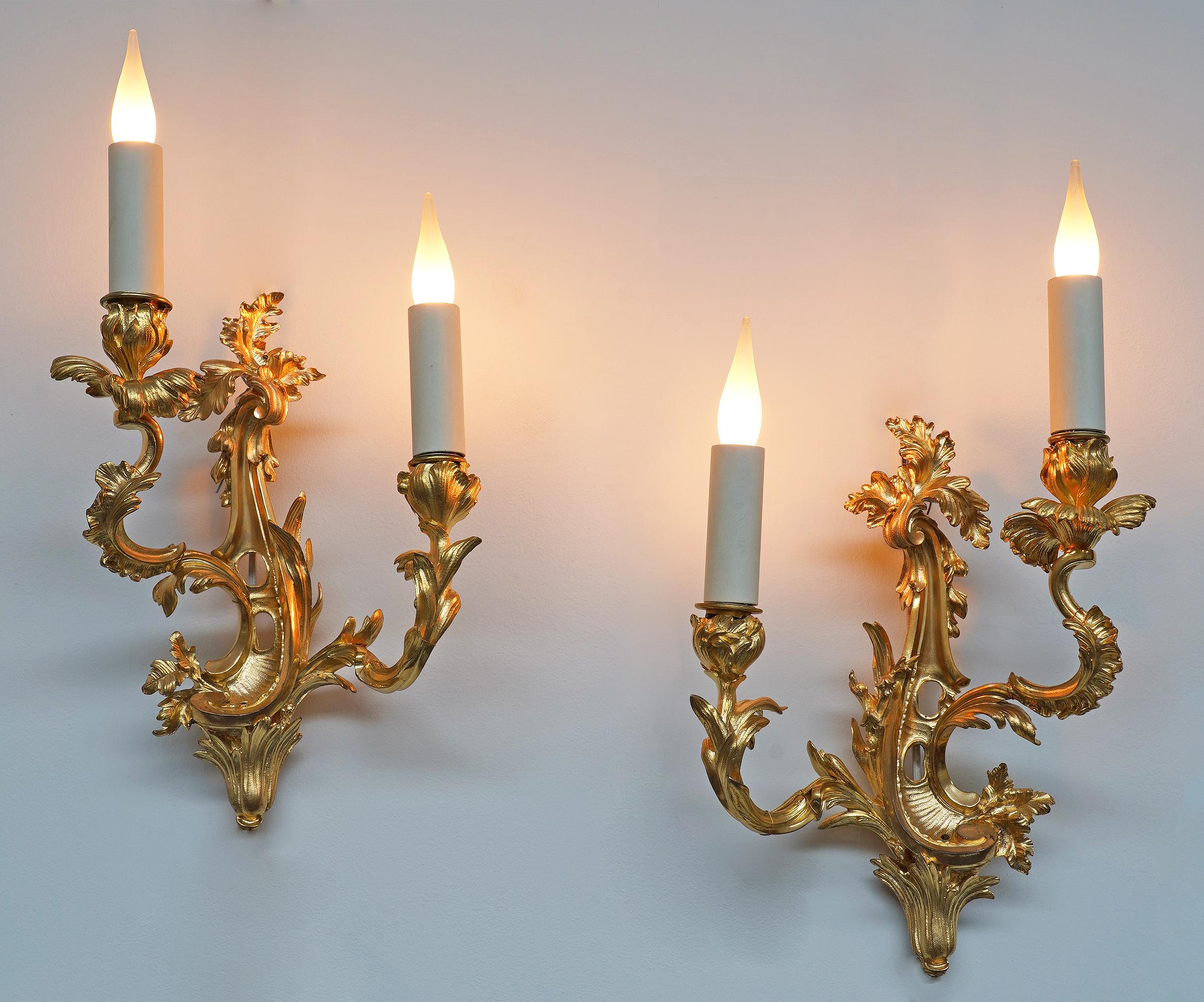 Höhe mit Beleuchtung : 42 cm (16,5 in.)

Charmantes Paar zweiflammiger Wandleuchten im Stil der Rocaille aus ziselierter, vergoldeter und durchbrochener Bronze.
Sie haben eine gewellte Form und sind mit zahlreichen Blättern und Schnörkeln