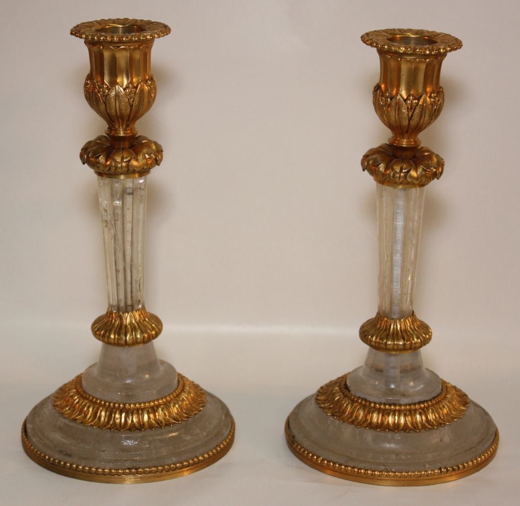 Pair of gilt bronze and rock crystal candlesticks, the tapered and fluted rock crystal shafts supporting the foliate candle nozzles, each raised on stepped crystal and bronze base.