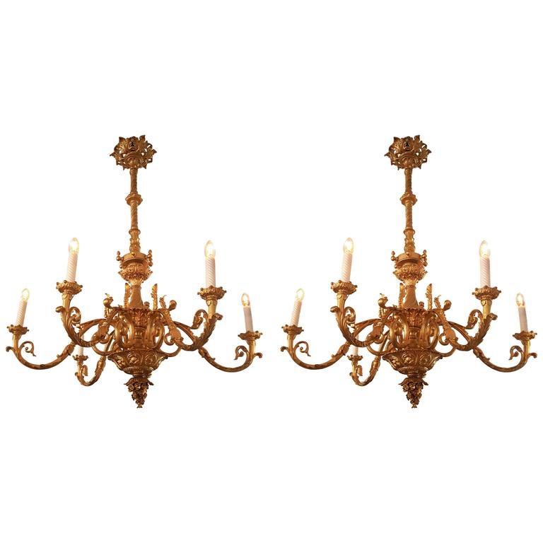 A pair of identical massive cast iron French chandeliers, each six flames, formerly run with natural gas, newly restored and electrified. 
Gold bronzed. The color of the glass candles can be adjusted due to your wish. 
Ornated Louis XV / Louis VIX