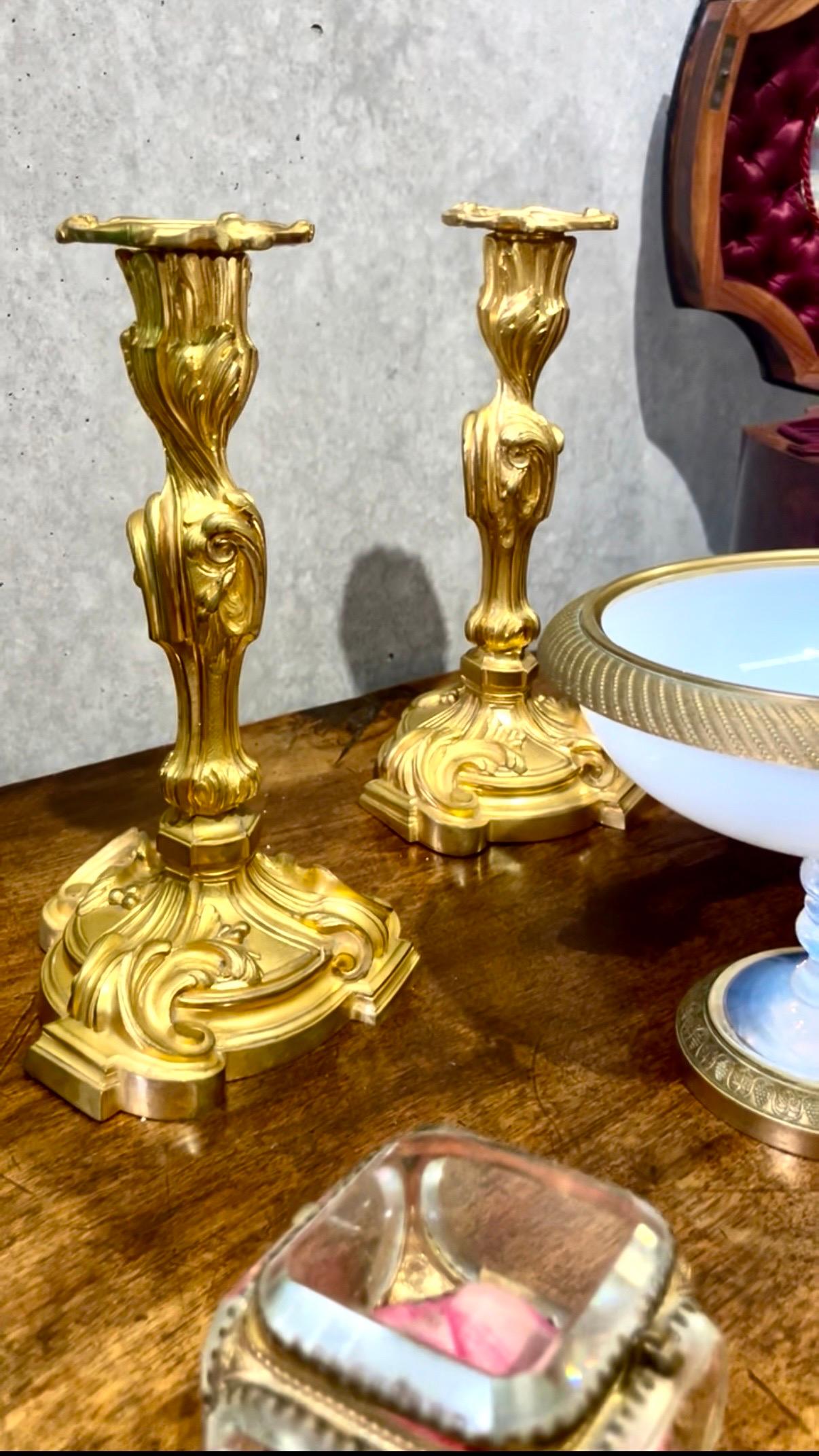 Questa elegante coppia di candelieri francesi in bronzo dorato incarna il sontuoso stile decorativo del XIX secolo, ispirandosi all'esuberante revival Rococo che fiorì durante il regno di Napoleone III. I candelieri sono riccamente fusi con