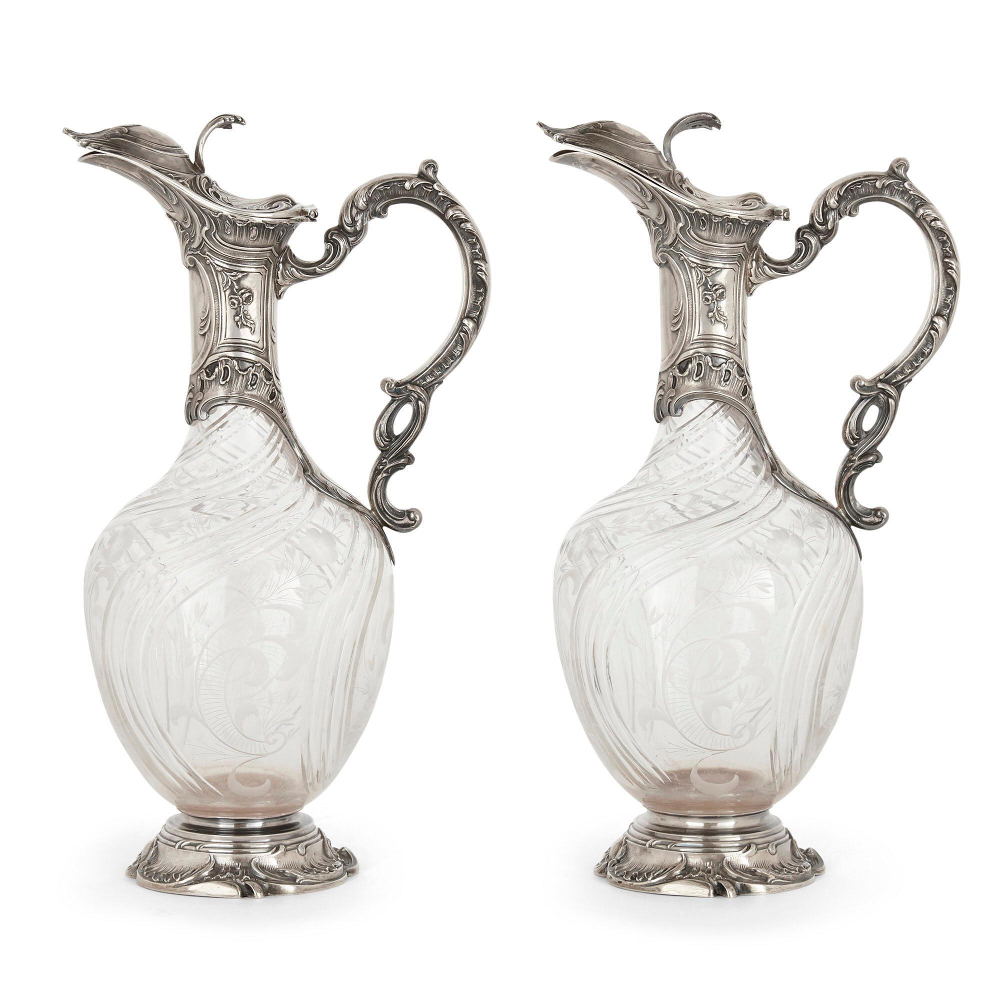 Pair of Rococo style cut glass and silver jugs by Charles Hack
French, early 20th century
Measures: Height 28cm, width 16cm, depth 11cm

Crafted in the charming Rococo Revival style from cut glass and silver, this pair of claret jugs is by the