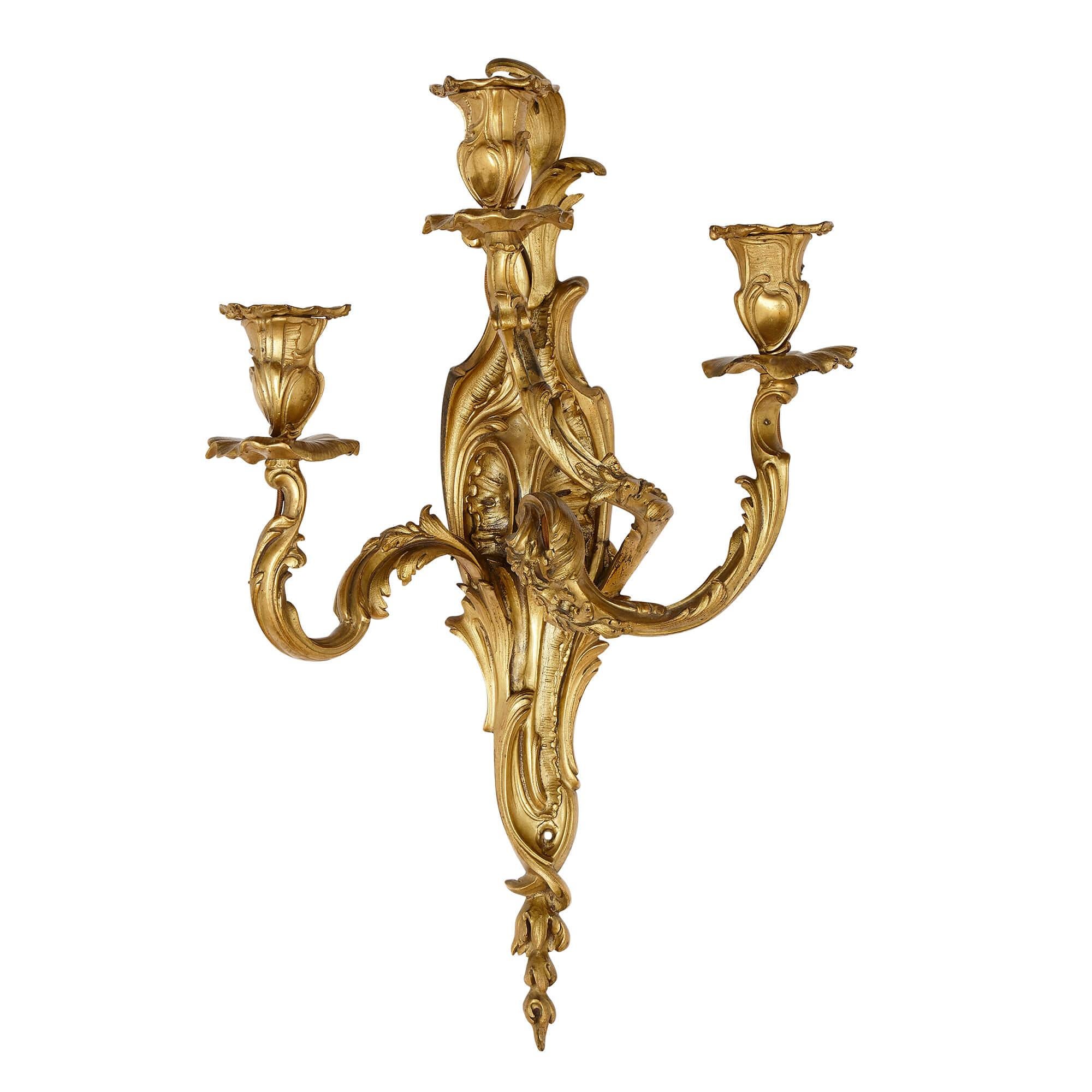 Pair of Rococo style gilt bronze sconces
French, 19th Century
Measures: Height 50cm, width 31cm, depth 16cm

This elegant pair of sconces beautifully demonstrates the Rococo, or Louis XV, style. Each gilt bronze sconce features an elongated