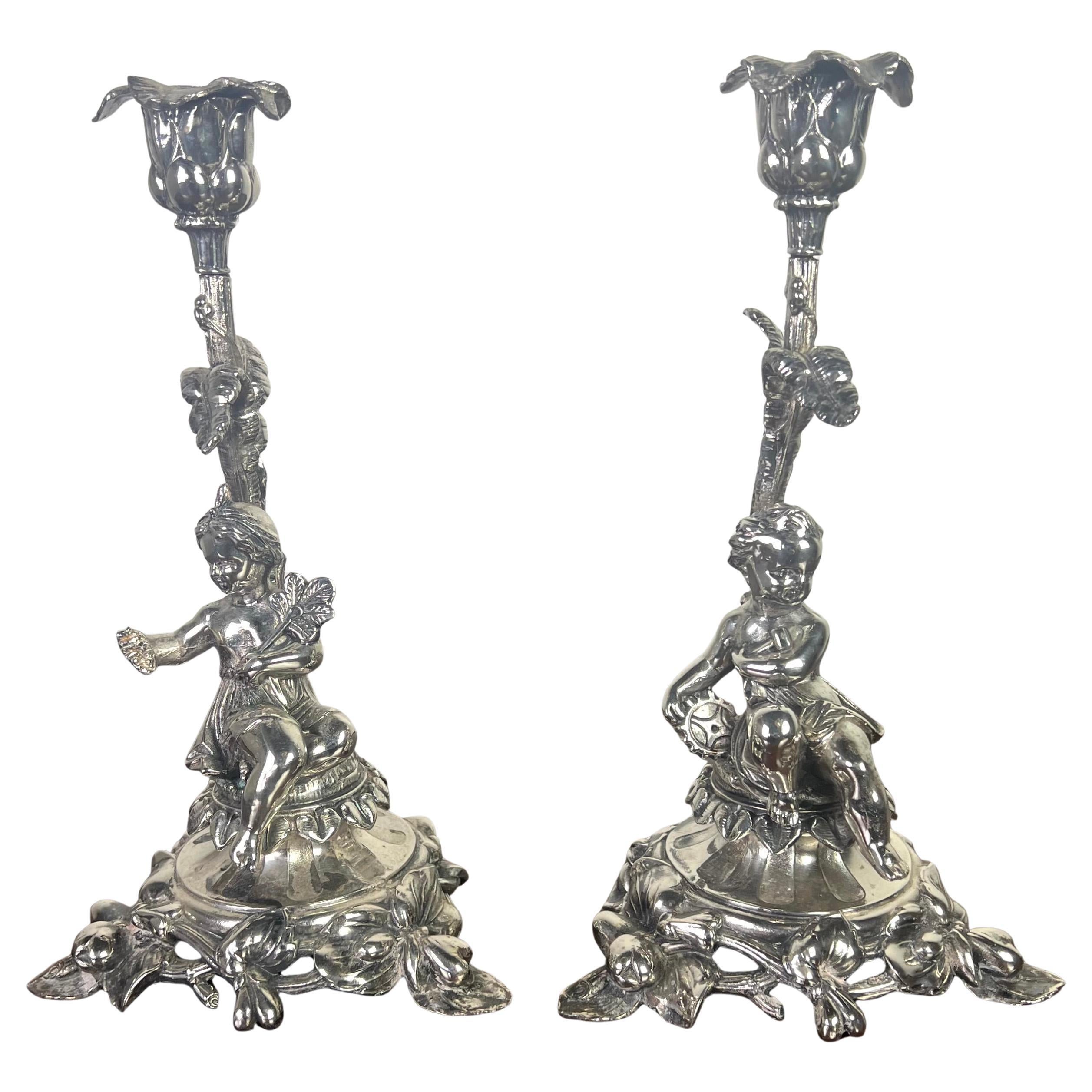 Pair of early 20th century Rococo style silver plated cherub candlesticks.  Each candlestick features a detailed cherub figure sitting on a sculptural base.  These figures are delicately crafted, showcasing lifelike expressions and poses.  The top