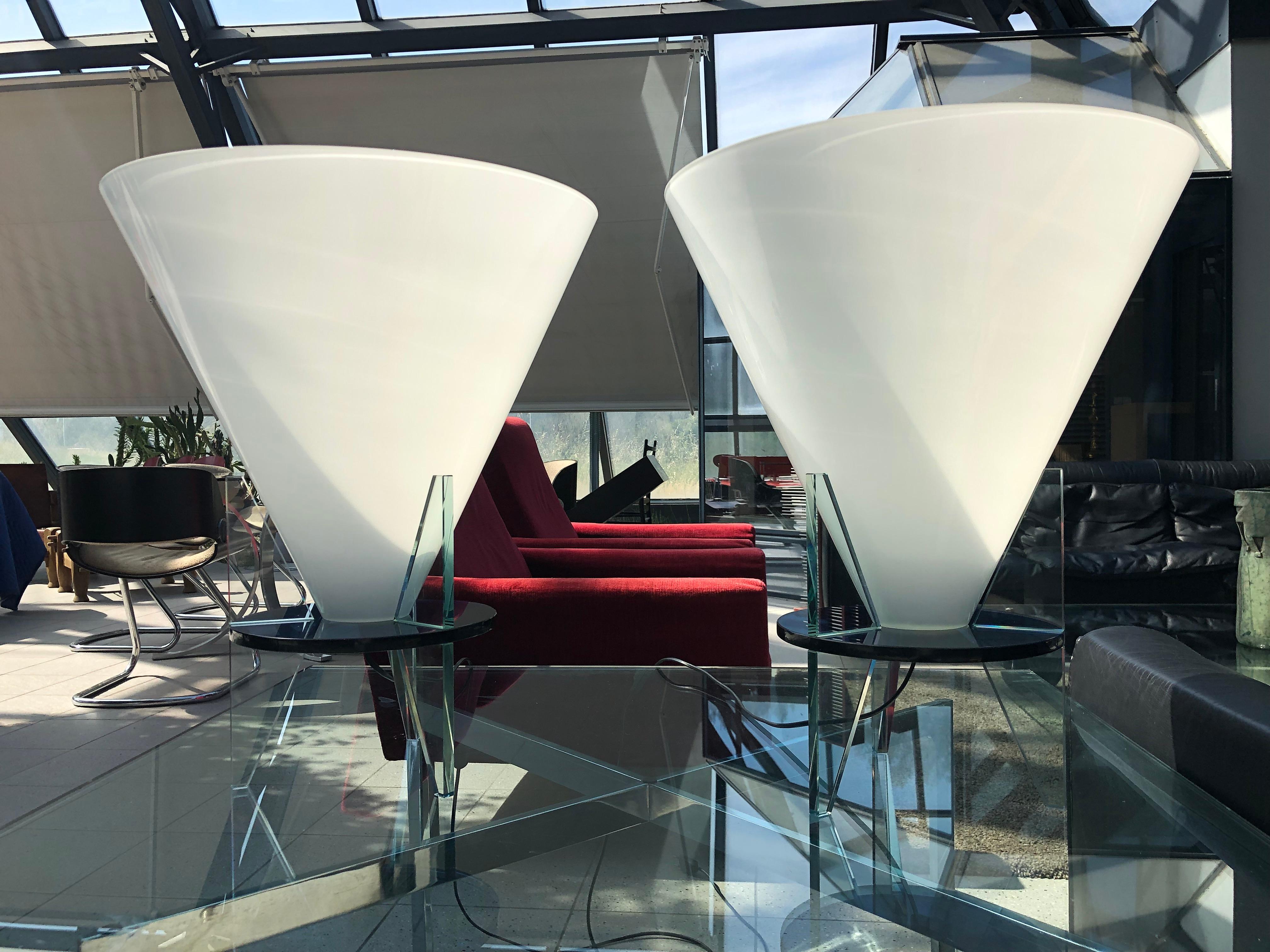 The inverted cone bulb cover in white opaline resting on a round black glass shelf with three legs in thick clear glass. Created in 1986, his lamps have not been published since 2005. Italian work.