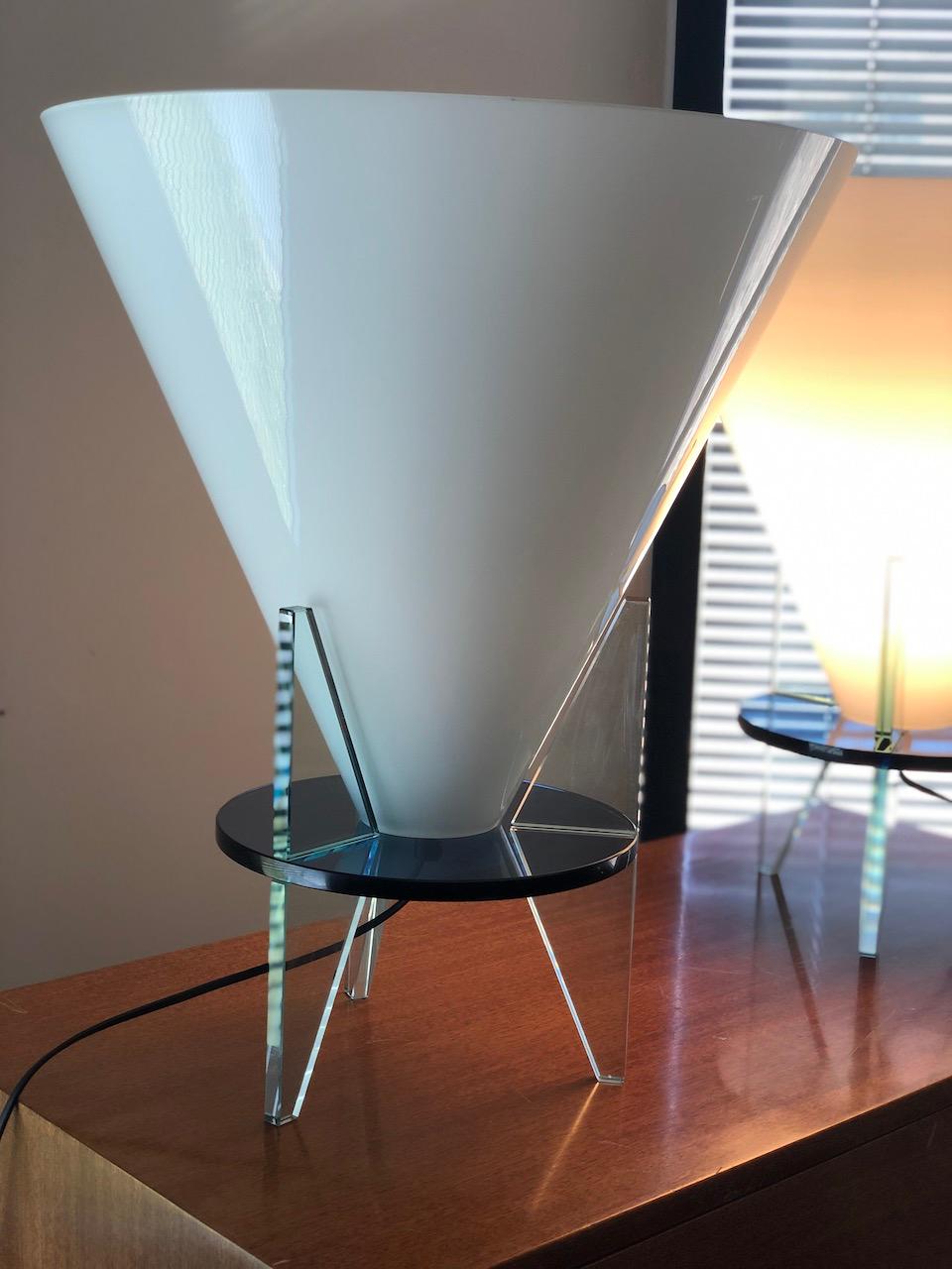 The white opaline inverted cone bulb cover resting on a round black glass shelf with three thick transparent glass legs. Created in 1986, this lamp has not been produced since 2005. Vintage Italian. Measures: height: 54 cm. diameter: 44 cm.
