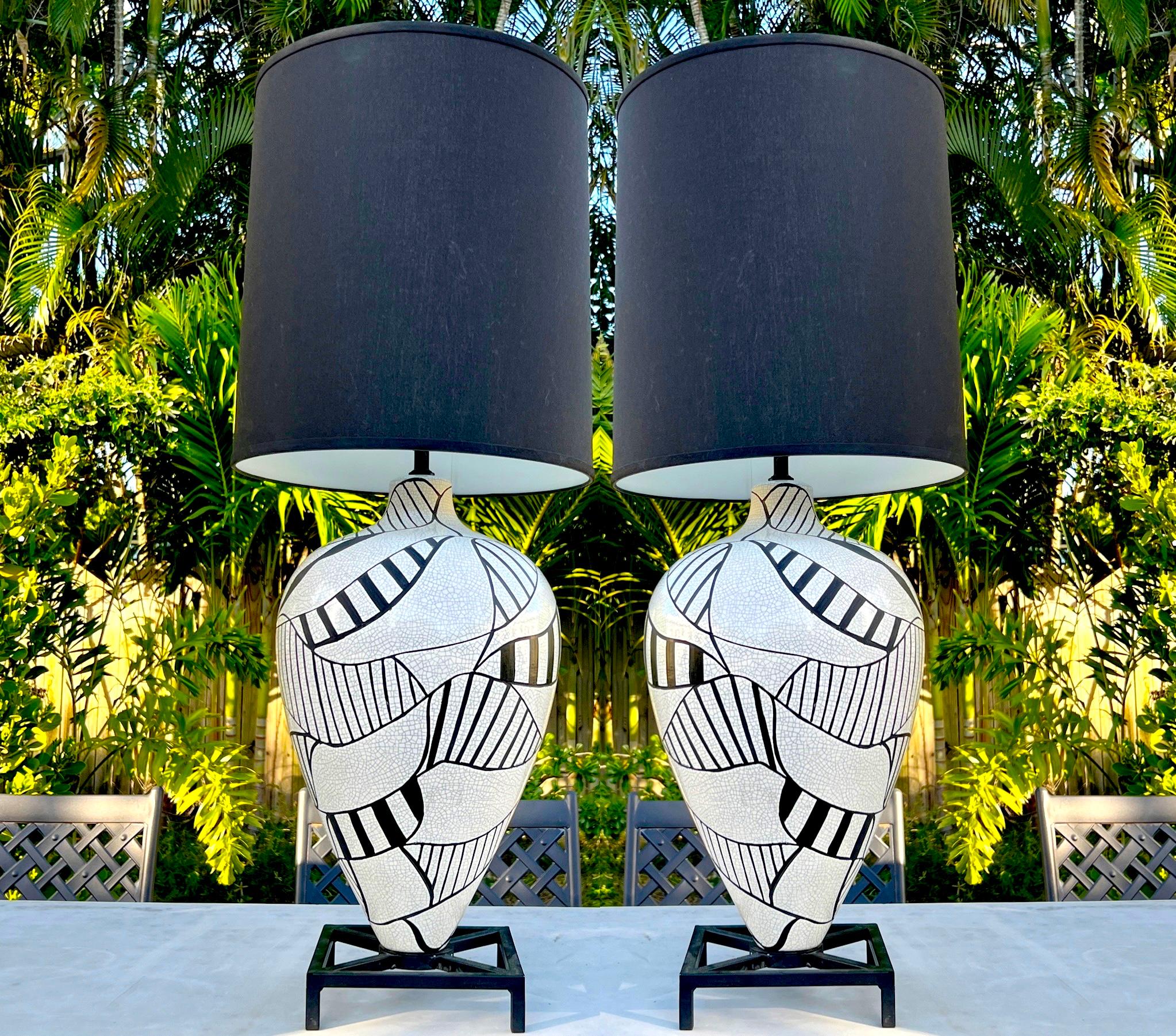Coppia di lampade moderniste in ceramica a forma di urna di grandi dimensioni con finitura in smalto bianco crepla e disegni geometrici dipinti a mano in smalto nero. Le lampade vintage poggiano su basi in ferro con piedi di colore nero. Le lampade